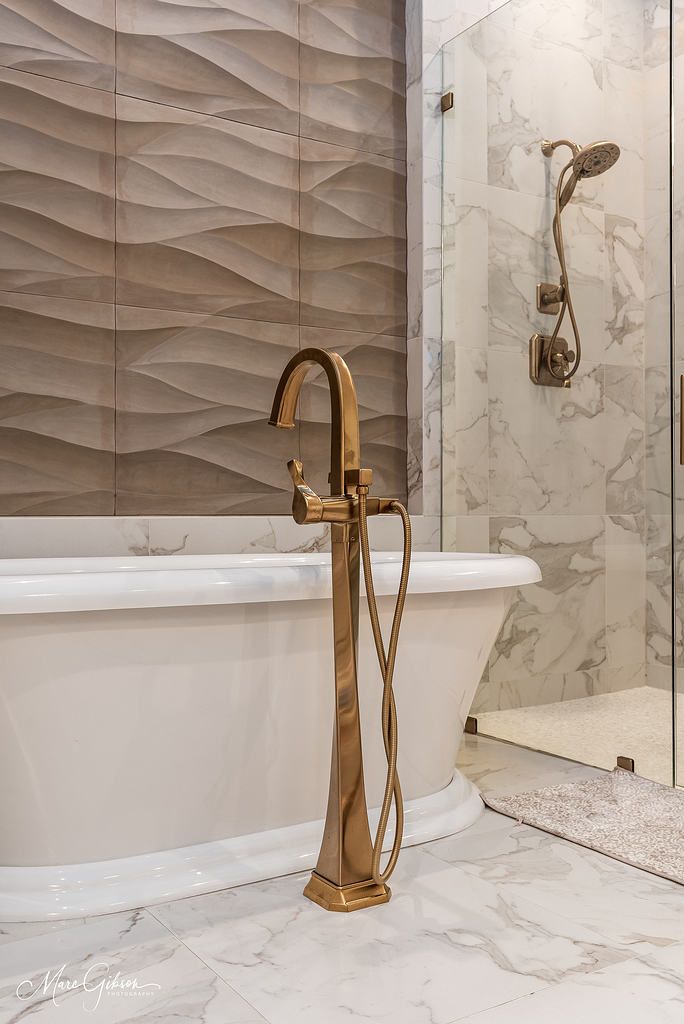 Luxury bathroom with white tub, gold freestanding faucet, and marble-patterned walls and floor