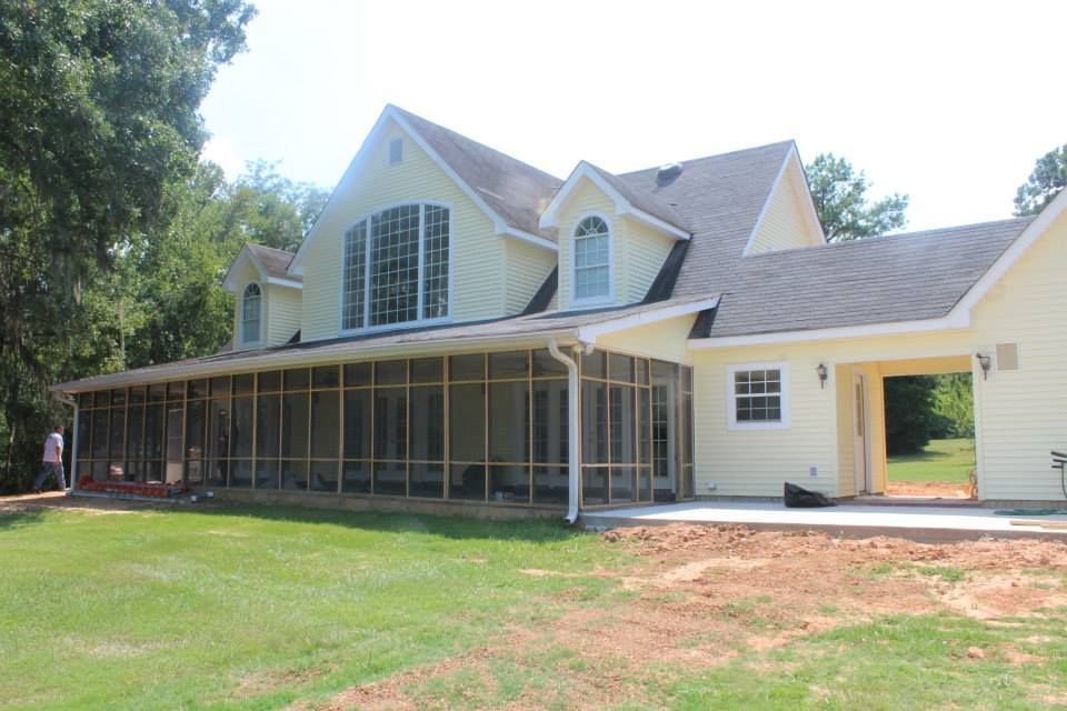 Yellow house with screened porch and dormer windows, surrounded by trees and a grassy yard