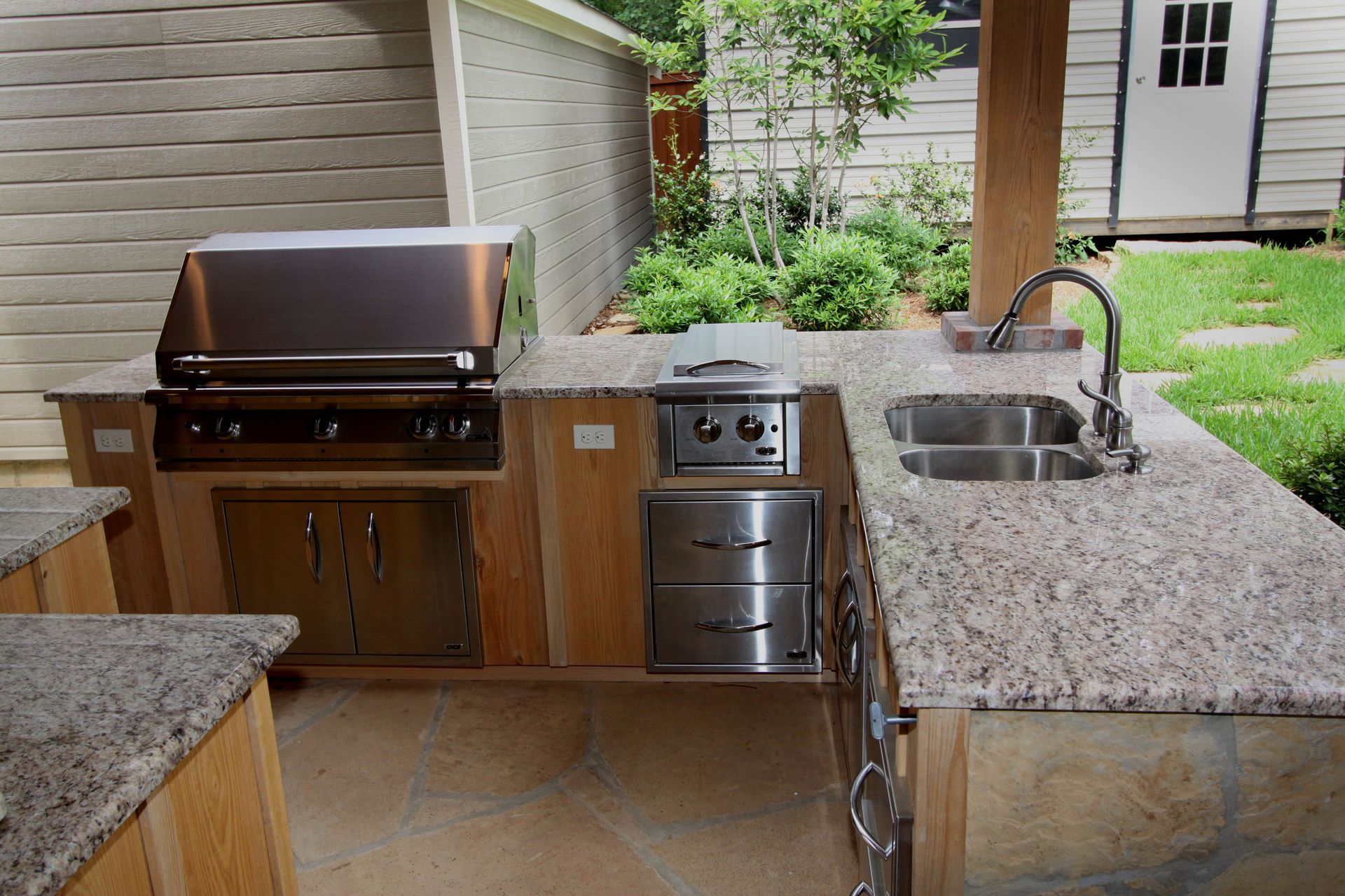 Outdoor built-in grill and sink with granite counter on a backyard patio