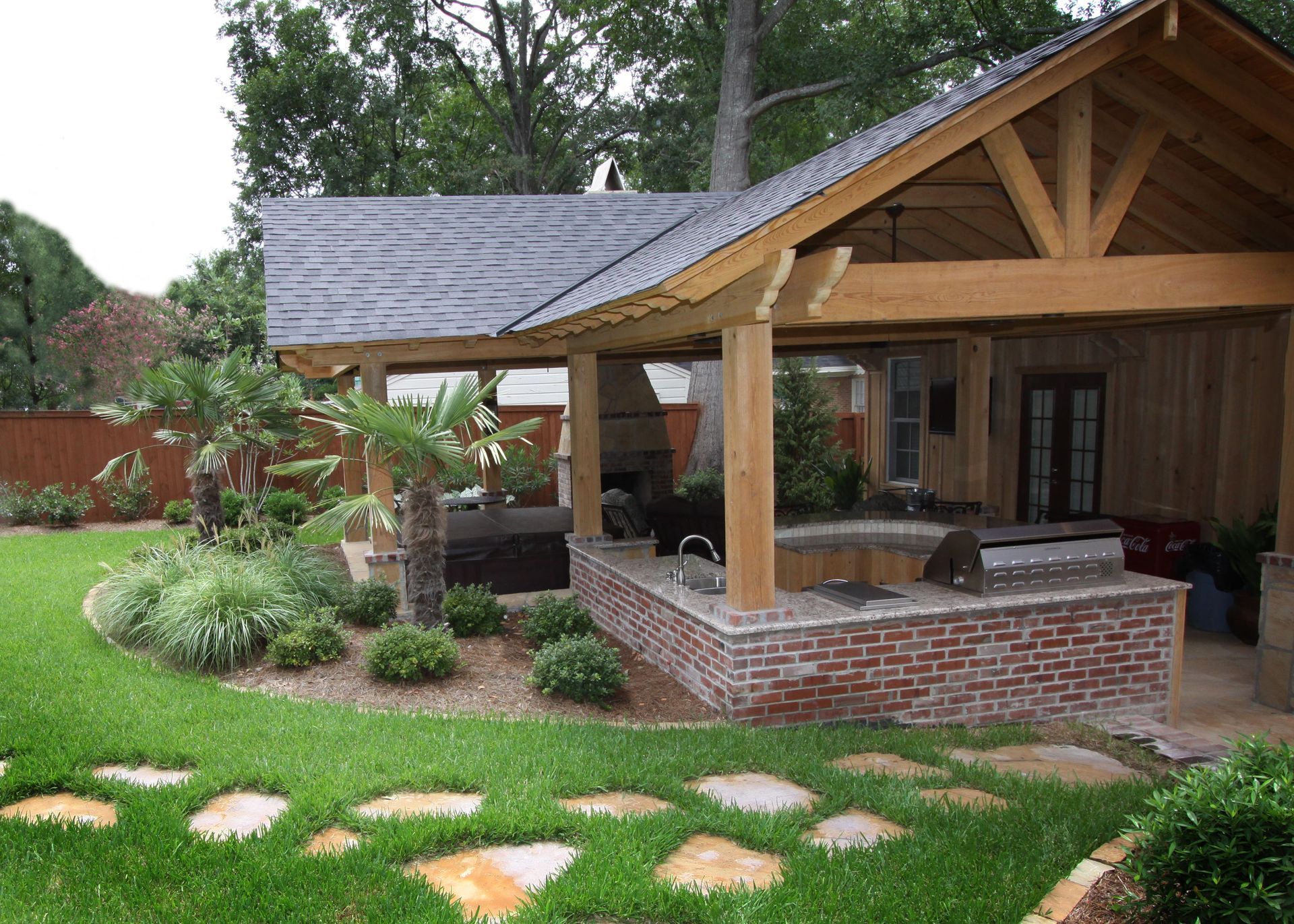 Brick house porch with wooden beams, landscaped yard, and stone stepping path
