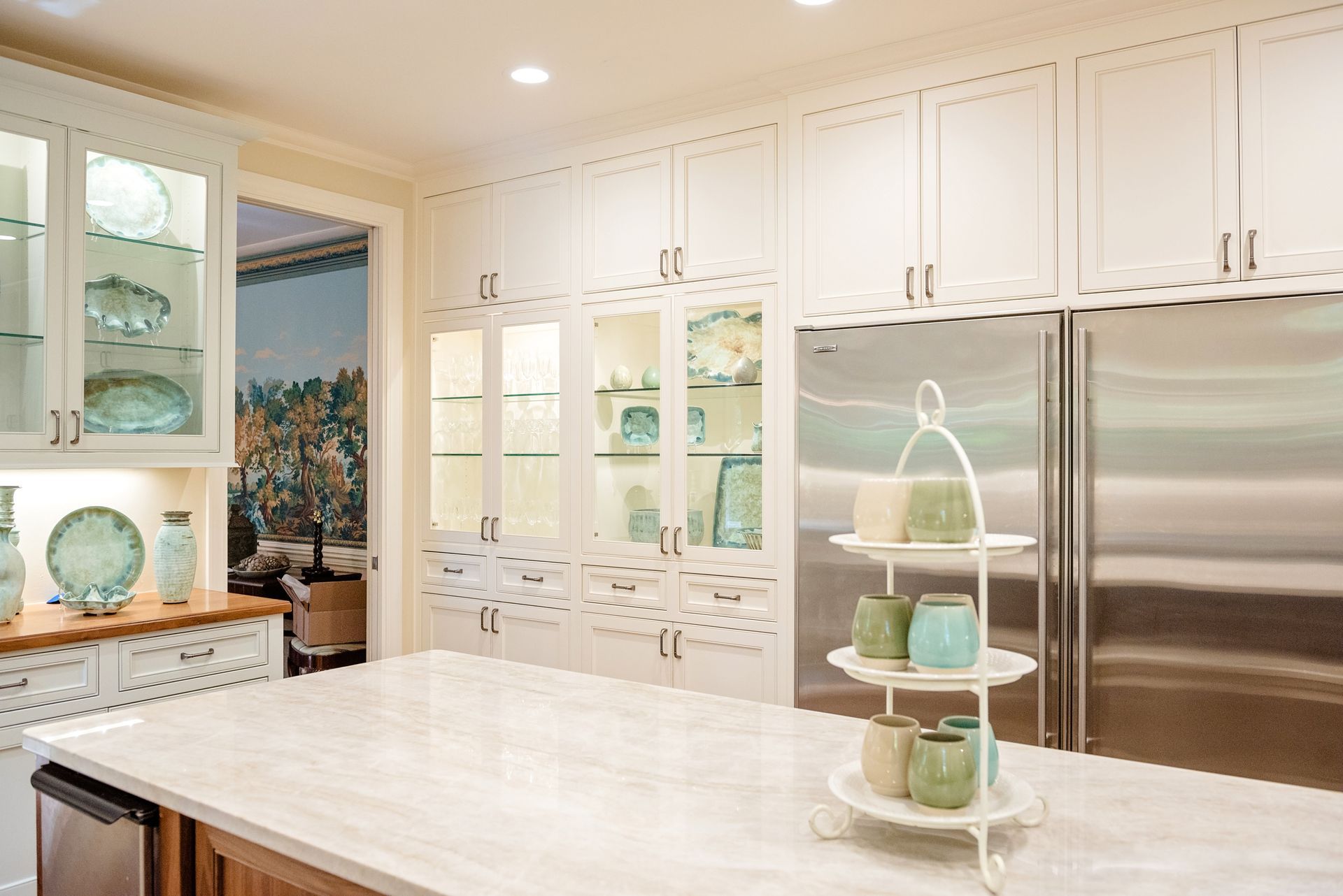Bright white kitchen with glass cabinets, marble island, and tiered tray centerpiece