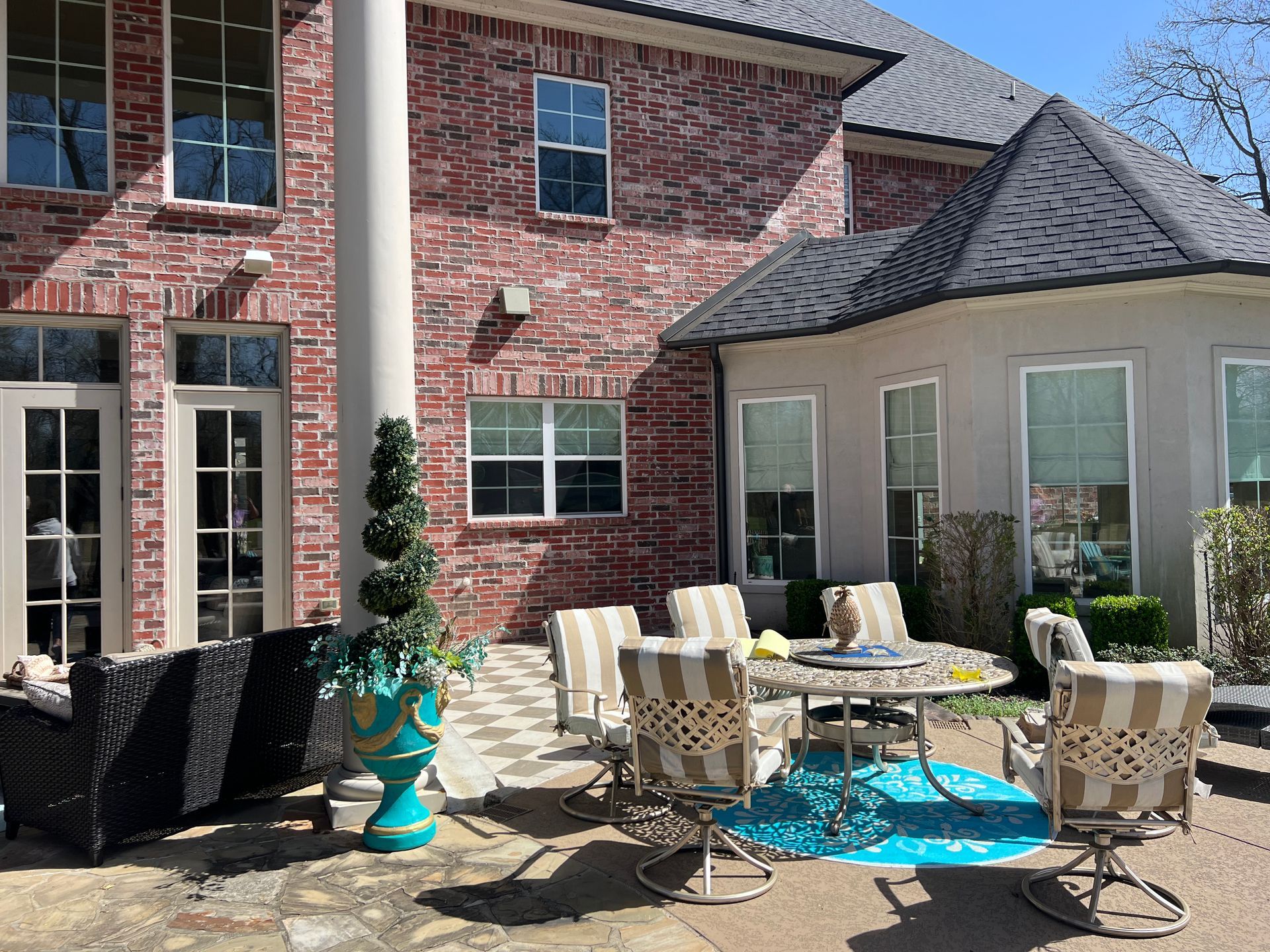 Patio with wicker chairs and table in front of a brick house and beige sunroom, with potted plants and turquoise decor