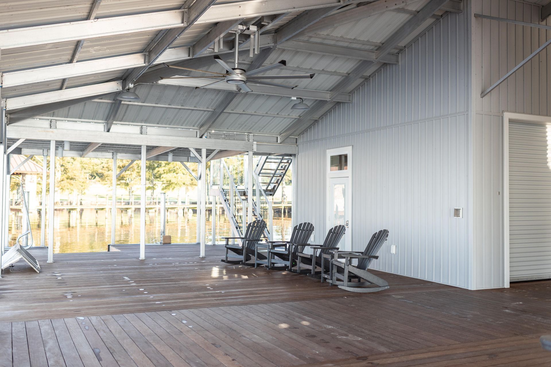 Covered wooden porch with metal roof, white siding, and several rocking chairs overlooking trees