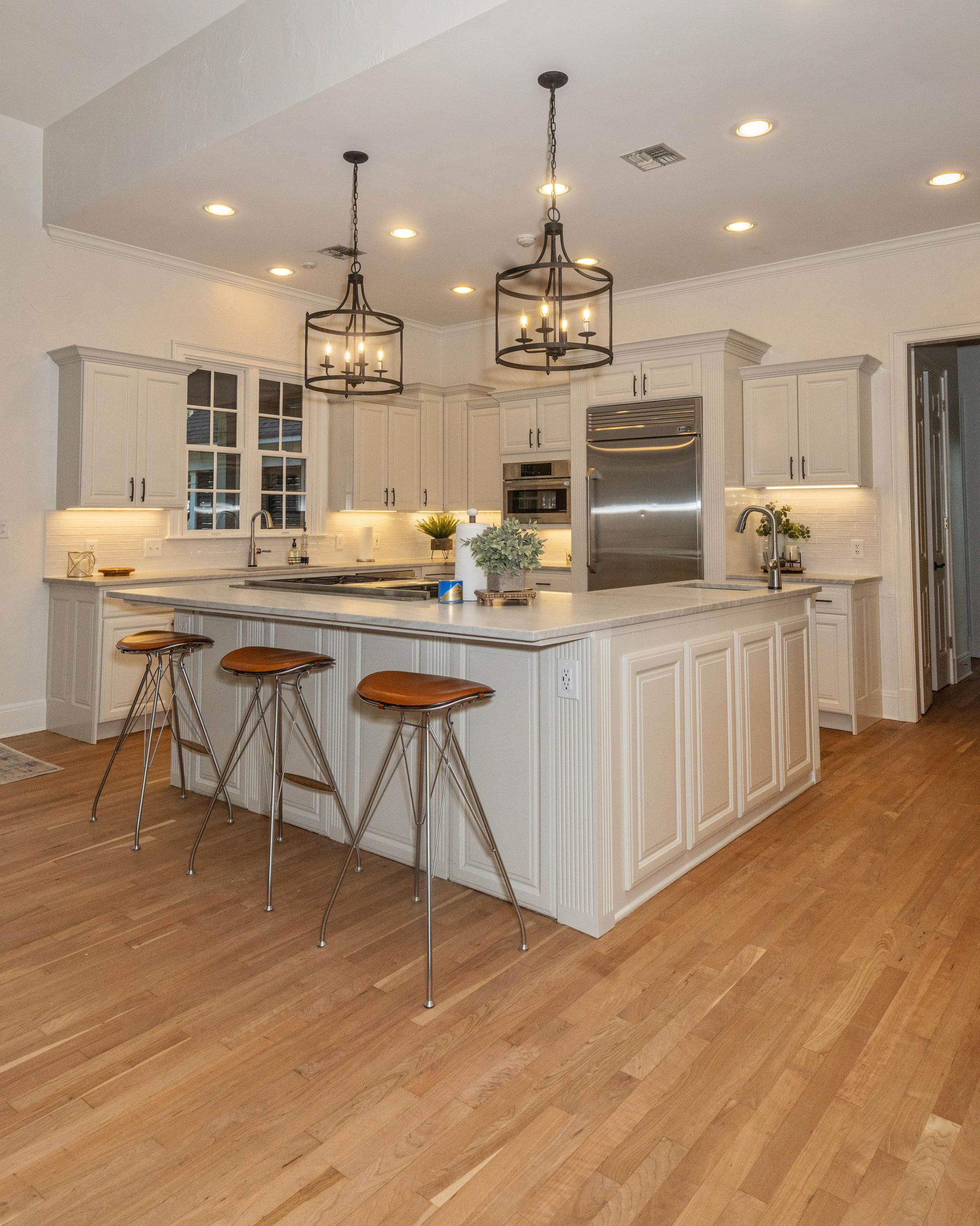 Bright modern kitchen with white cabinets, island seating, pendant lights, and hardwood floors