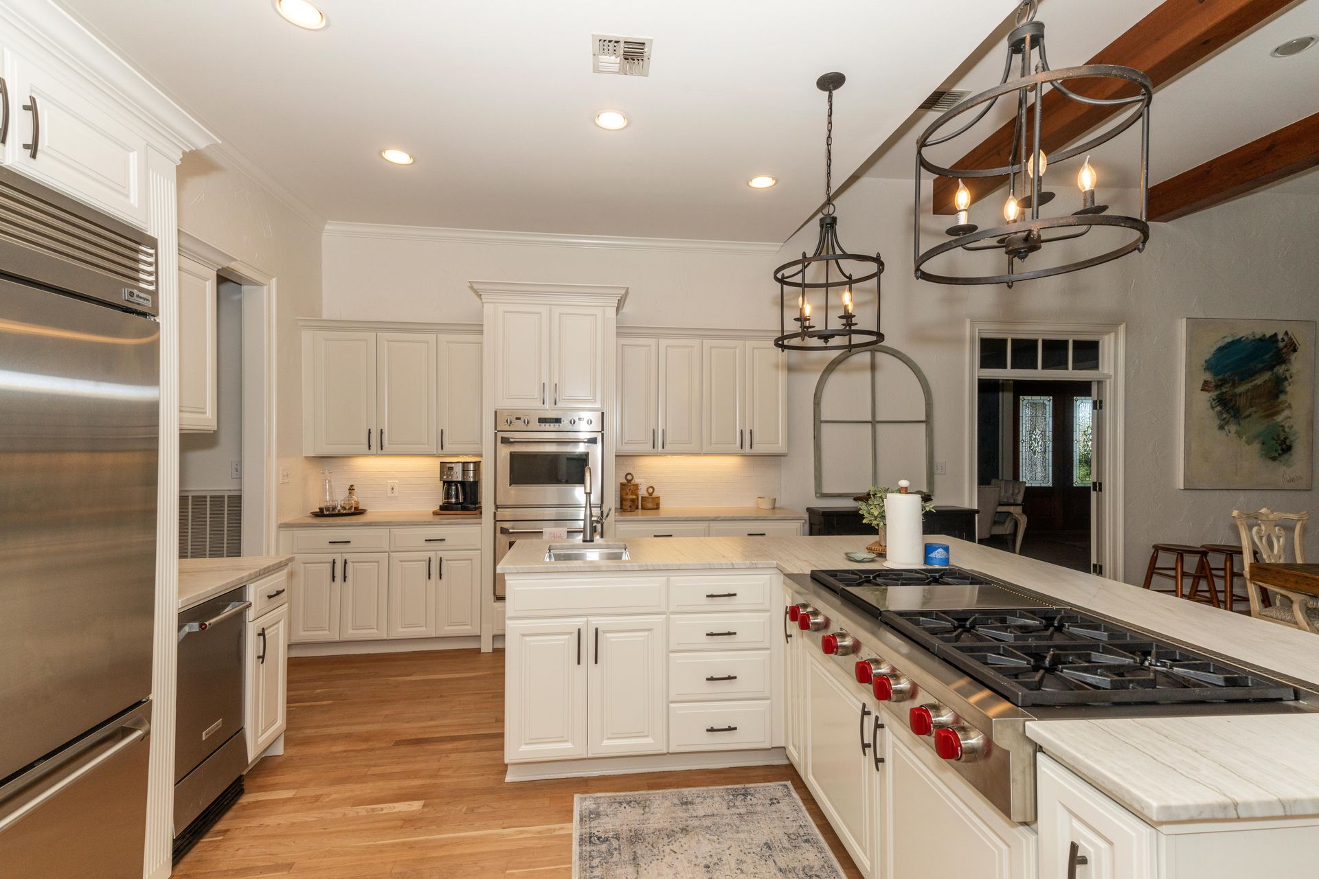 Bright white kitchen with stainless steel appliances, large island, and dark pendant lights