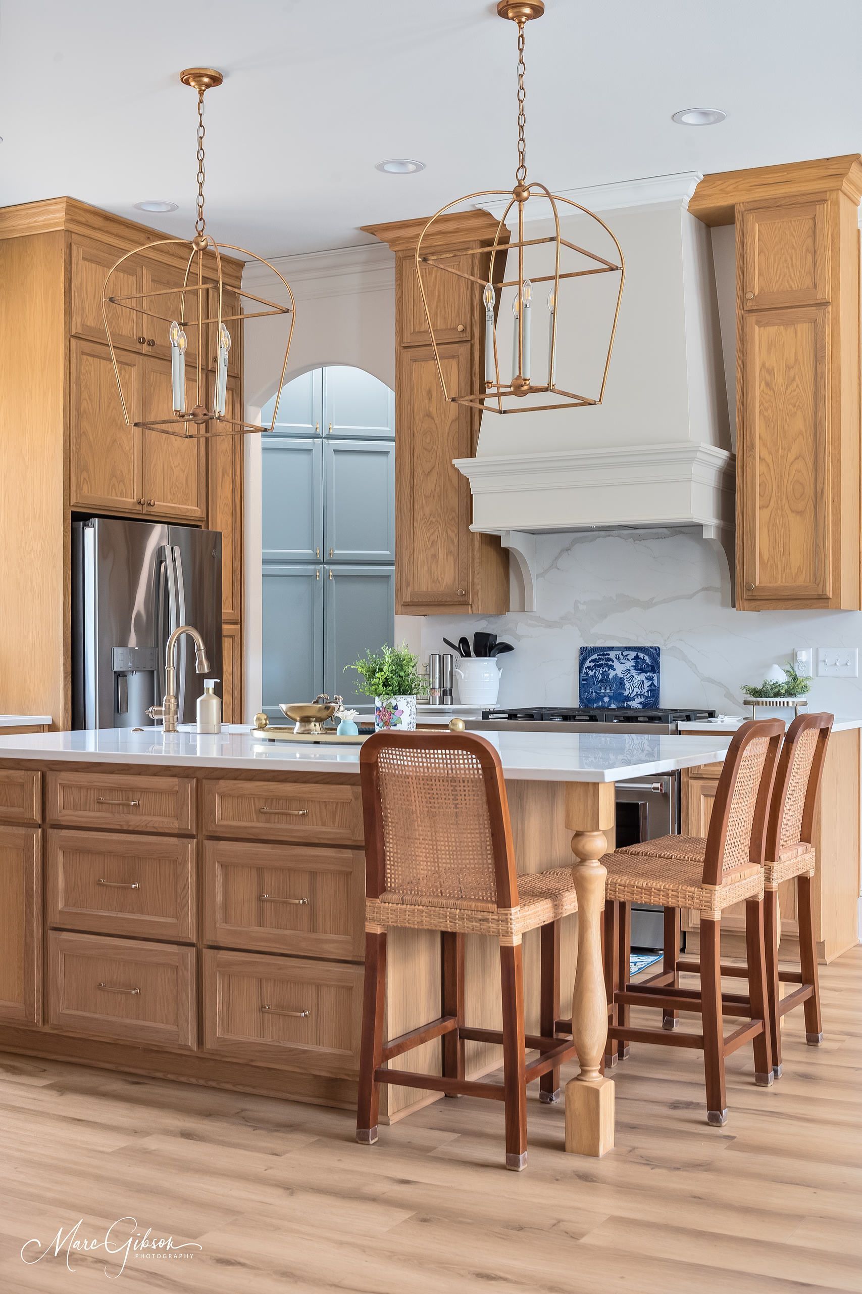 Modern kitchen with wooden cabinets, island seating, stainless refrigerator, and white range hood