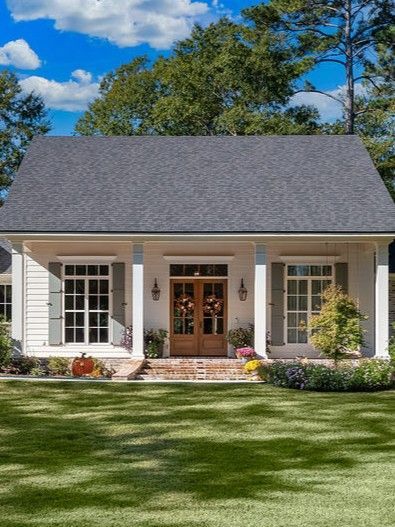 White house with gray roof, front porch, and wooden double doors, set in a sunny green yard under a blue sky