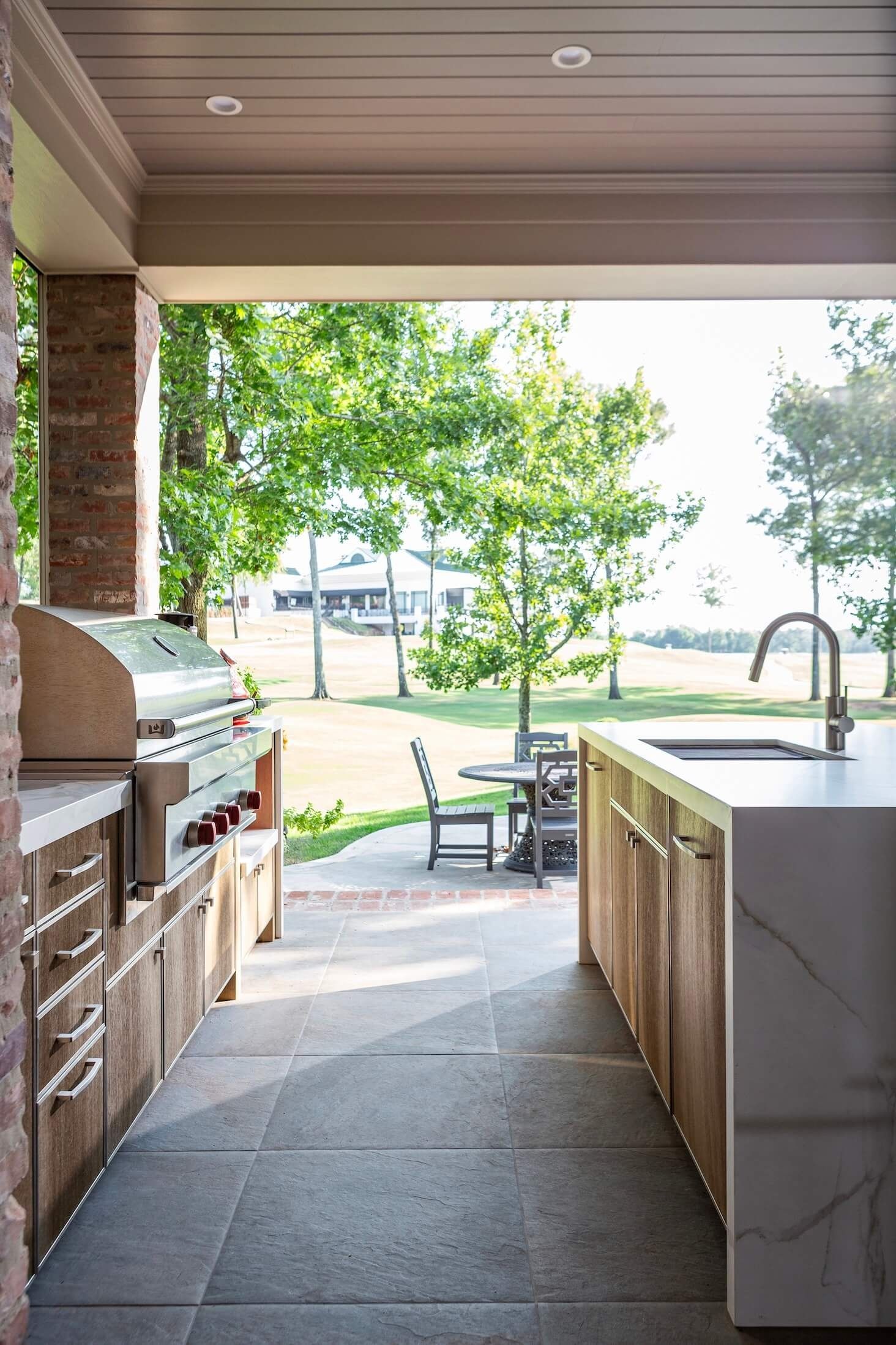 Outdoor kitchen patio with grill, sink island, and view of a sunlit backyard by the water