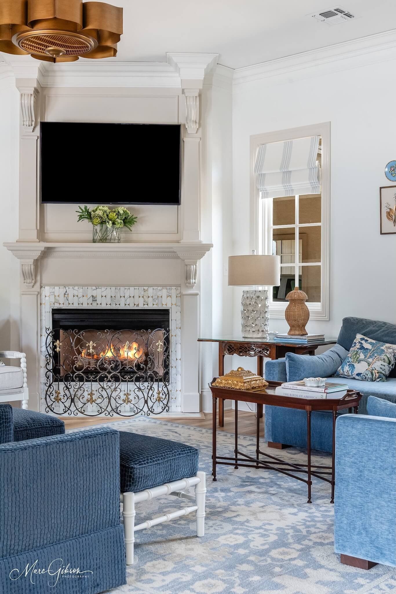 Elegant living room with a lit fireplace, mounted TV, blue seating, and a decorative mirror.