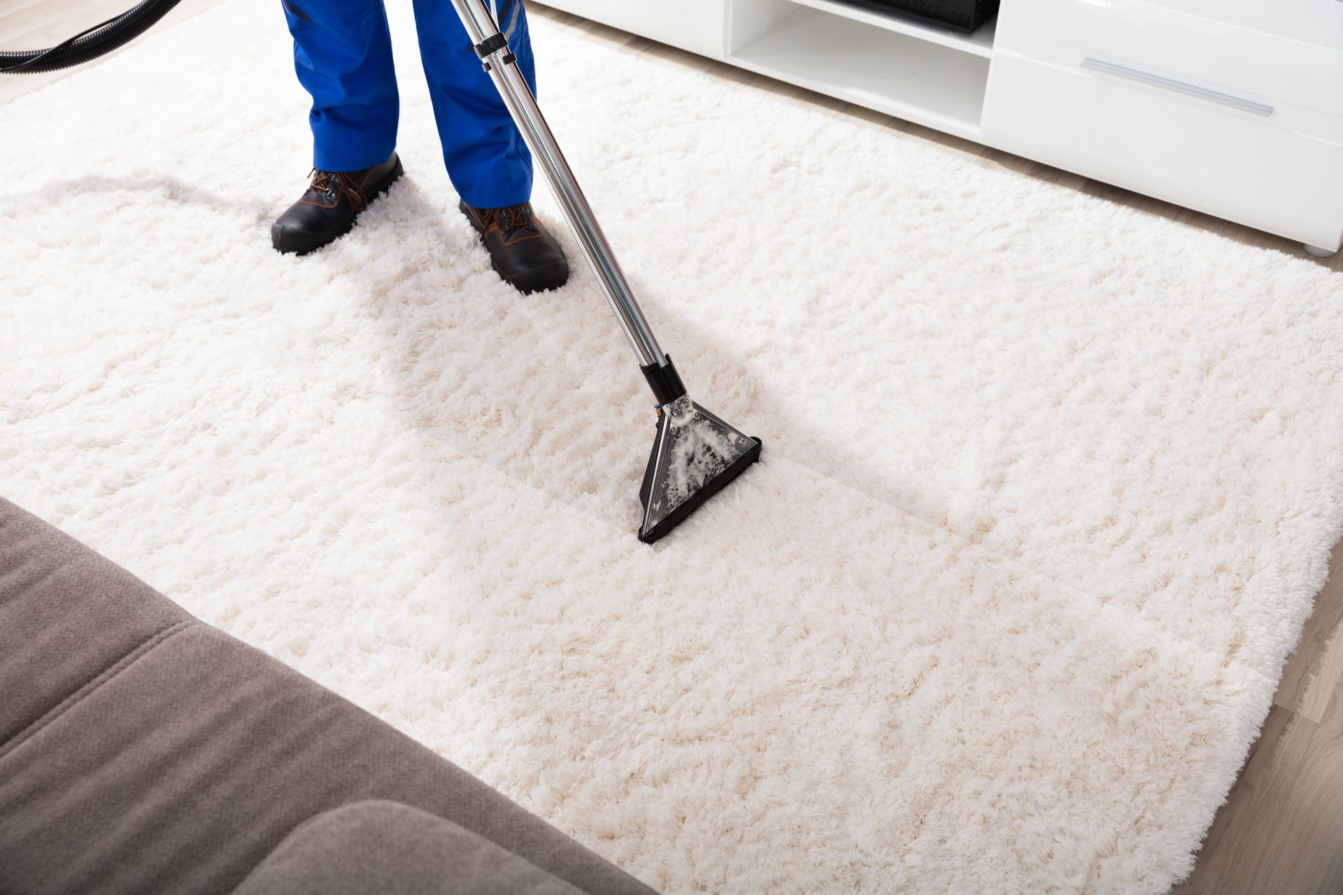 A person is using a vacuum cleaner to clean a white rug in a living room.