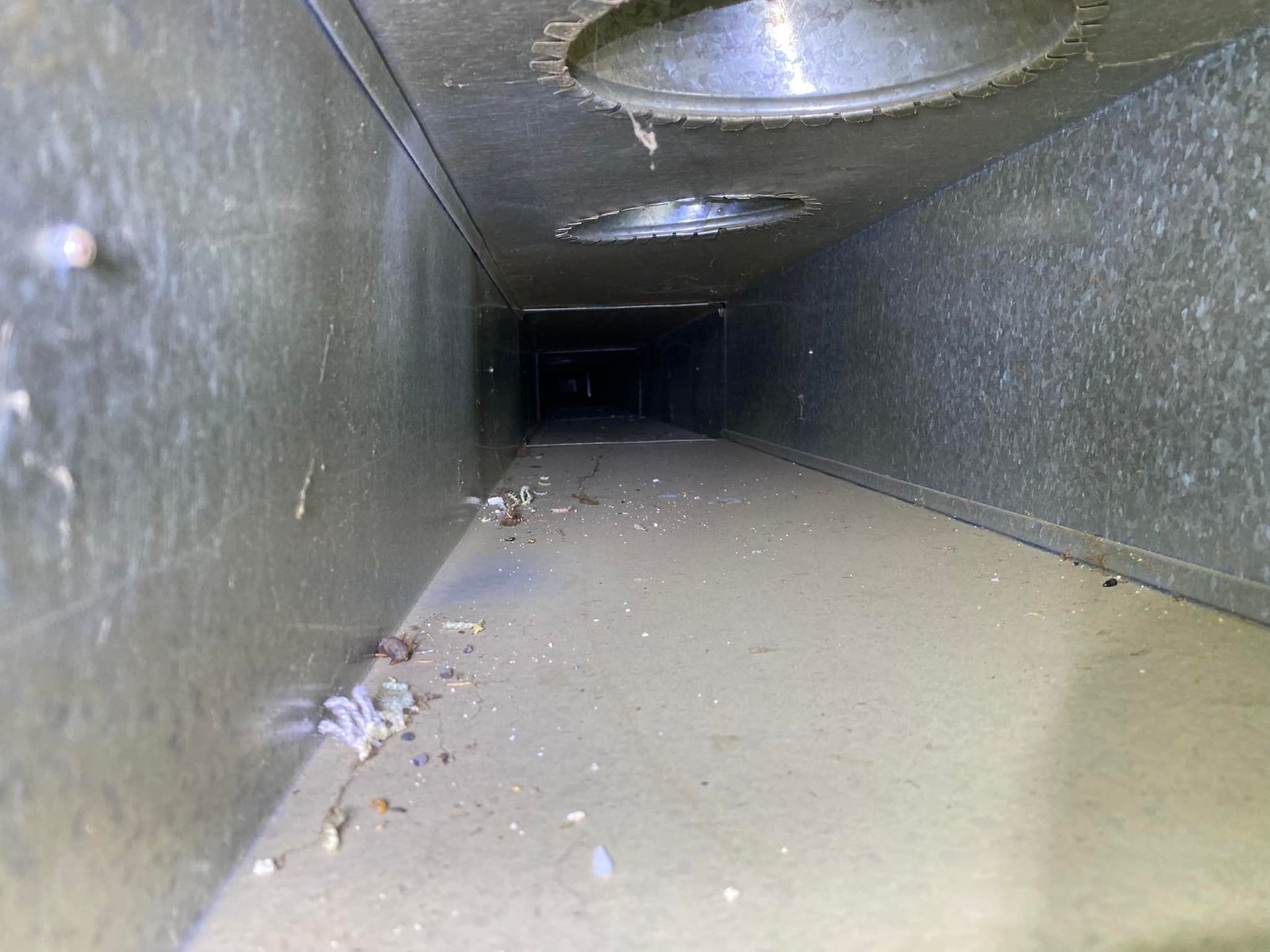 A dirty air duct with a lot of dust on the floor.