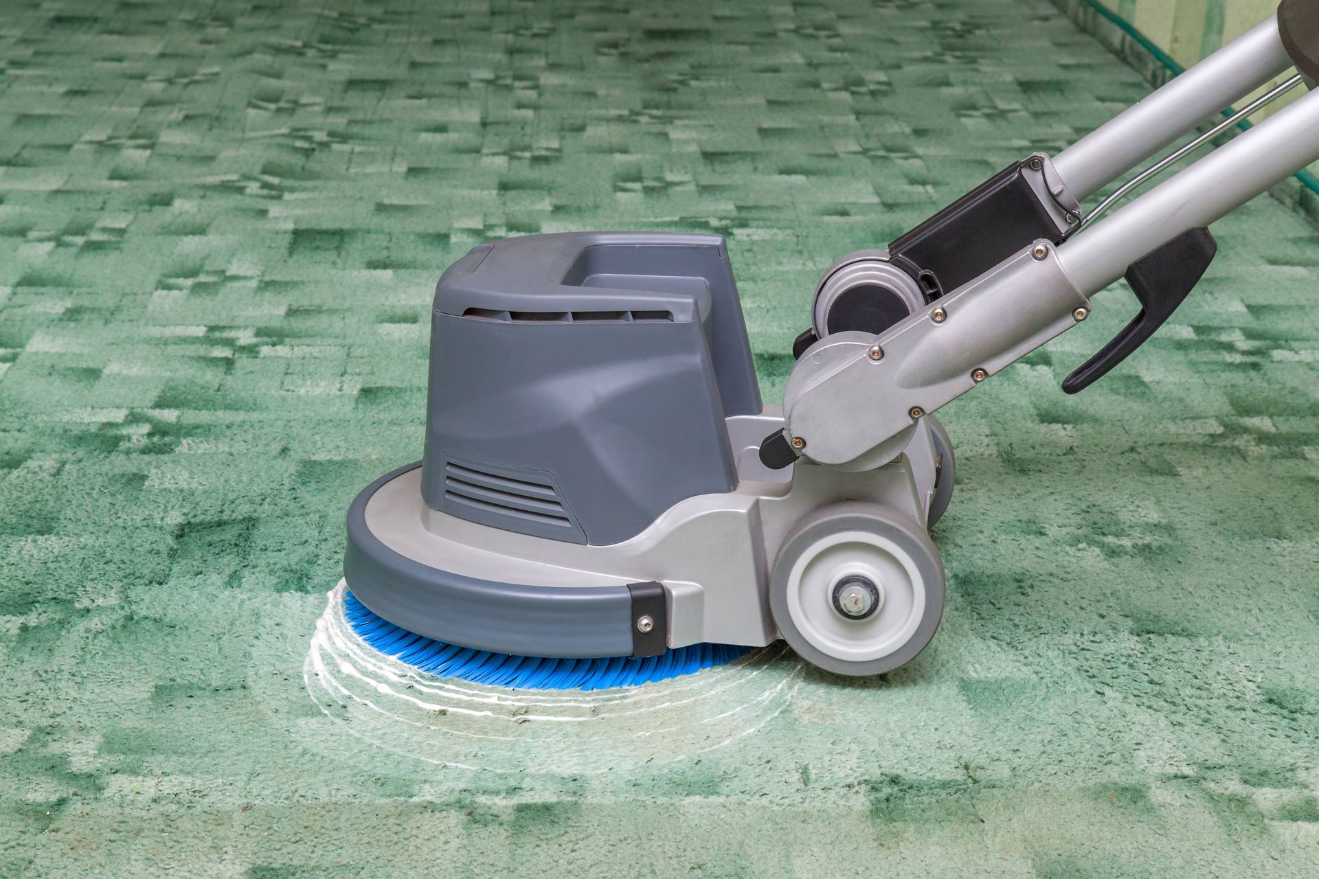 A person is using a machine to clean a green carpet.