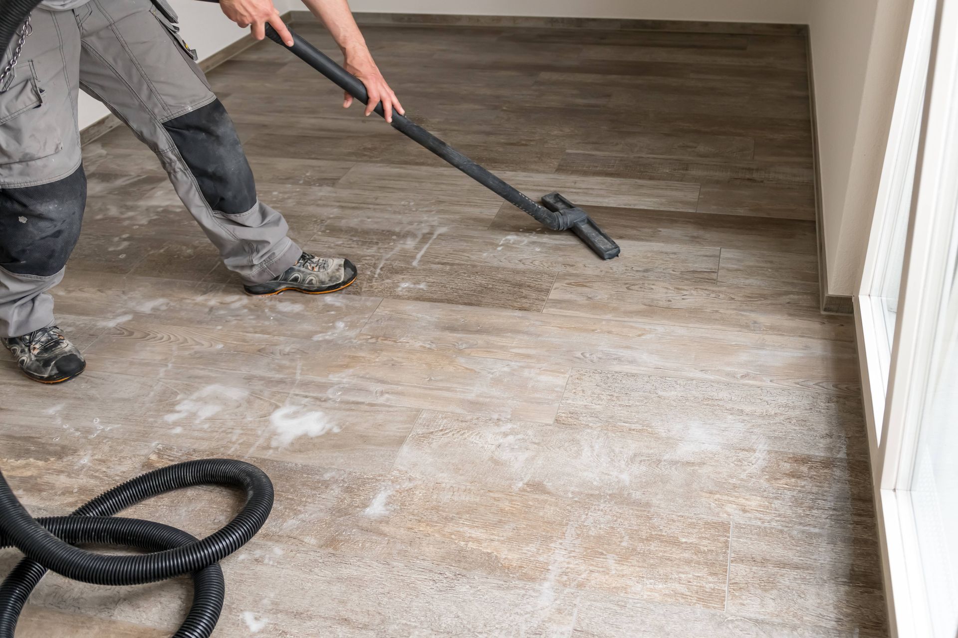 A man is using a vacuum cleaner to clean a wooden floor.