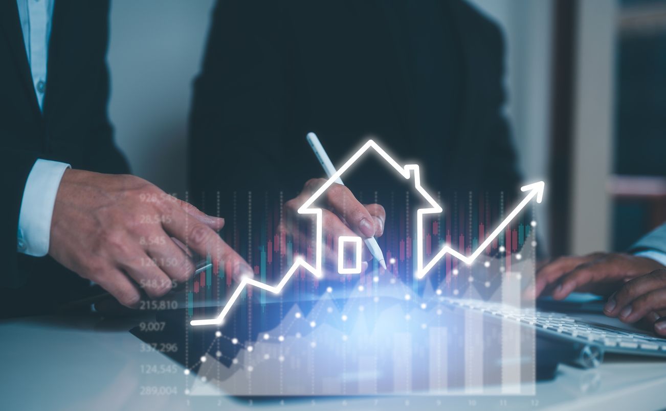 Personas con traje analizando un gráfico inmobiliario brillante con un ícono de casa, señalando una tableta y una línea ascendente.