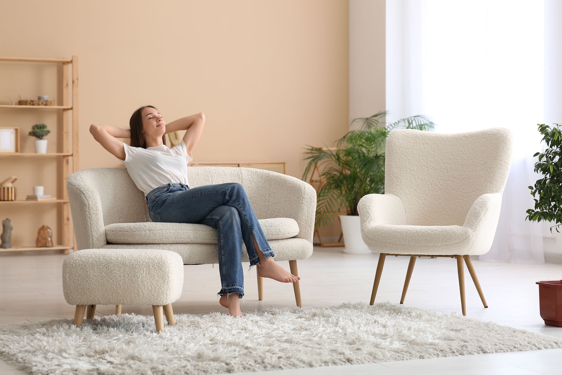 Frau entspannt sich auf einem cremefarbenen Sofa und lächelt mit den Händen hinter dem Kopf.