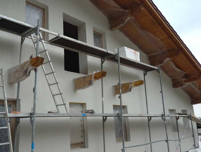 Gerüst an der Außenseite eines weißen Hauses während Renovierungsarbeiten, mit Leiter und überdachtem Dach.