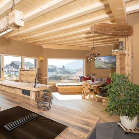 Geräumiger, holzgetäfelter Innenraum mit Küche, Essbereich und großen Fenstern mit Blick auf die Stadt und die Berge.