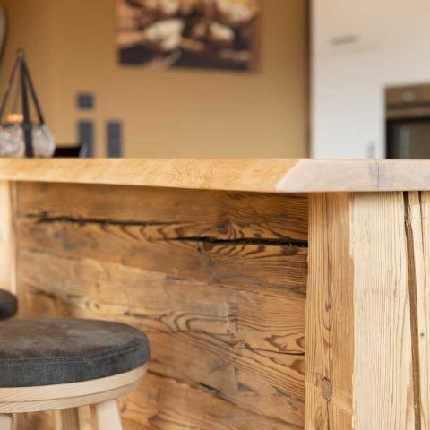 Holzbar mit Barhocker in einer Küche. Die Bar besteht aus Altholz, im Hintergrund hängt ein Gemälde.