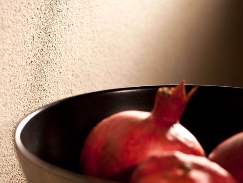 Schwarze Schale mit Granatäpfeln vor einer strukturierten braunen Wand.