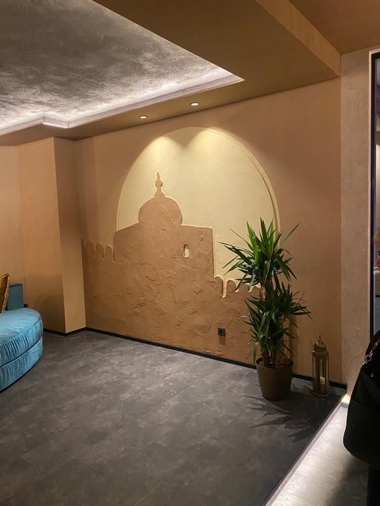 Innenraum mit strukturierter Wand mit Gebäudesilhouette, Pflanze und blaugrünen Sitzgelegenheiten.