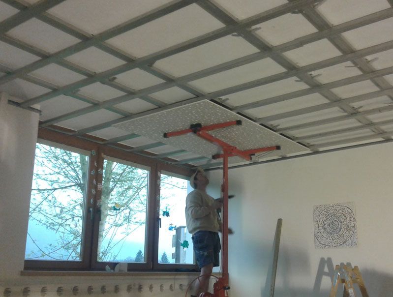 Mann, der in einem Raum mit einem Fenster steht und Deckenplatten mithilfe eines Aufzugs installiert.