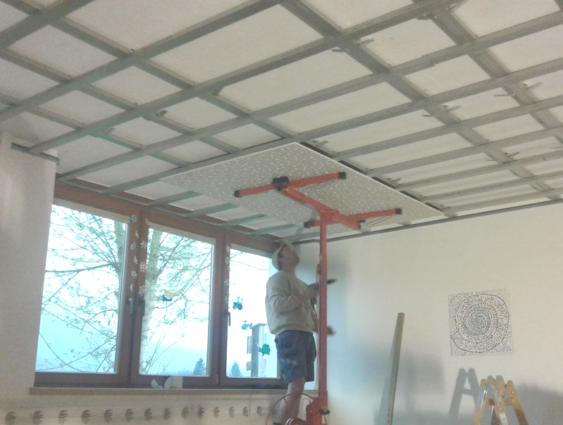 Person, die mit einem Hebewerkzeug eine Trockenbaudecke an der Decke installiert.