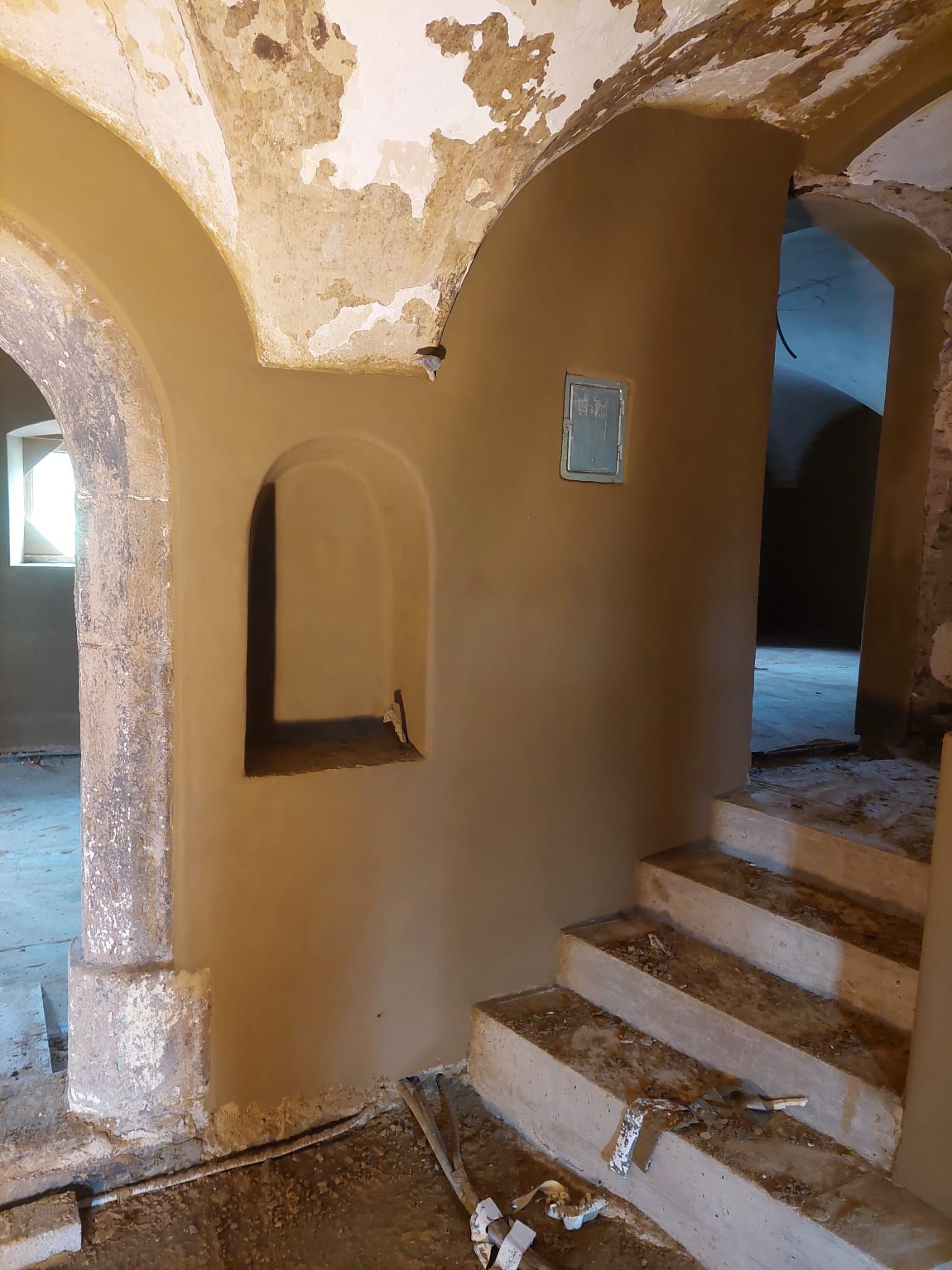 Innenansicht eines renovierten Gebäudes mit hellbraunen Wänden, gewölbten Türen und einer kleinen Treppe.