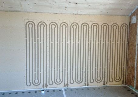 Wand mit eingebetteten, mäanderförmigen Heizrohren vor der Trockenbaumontage.