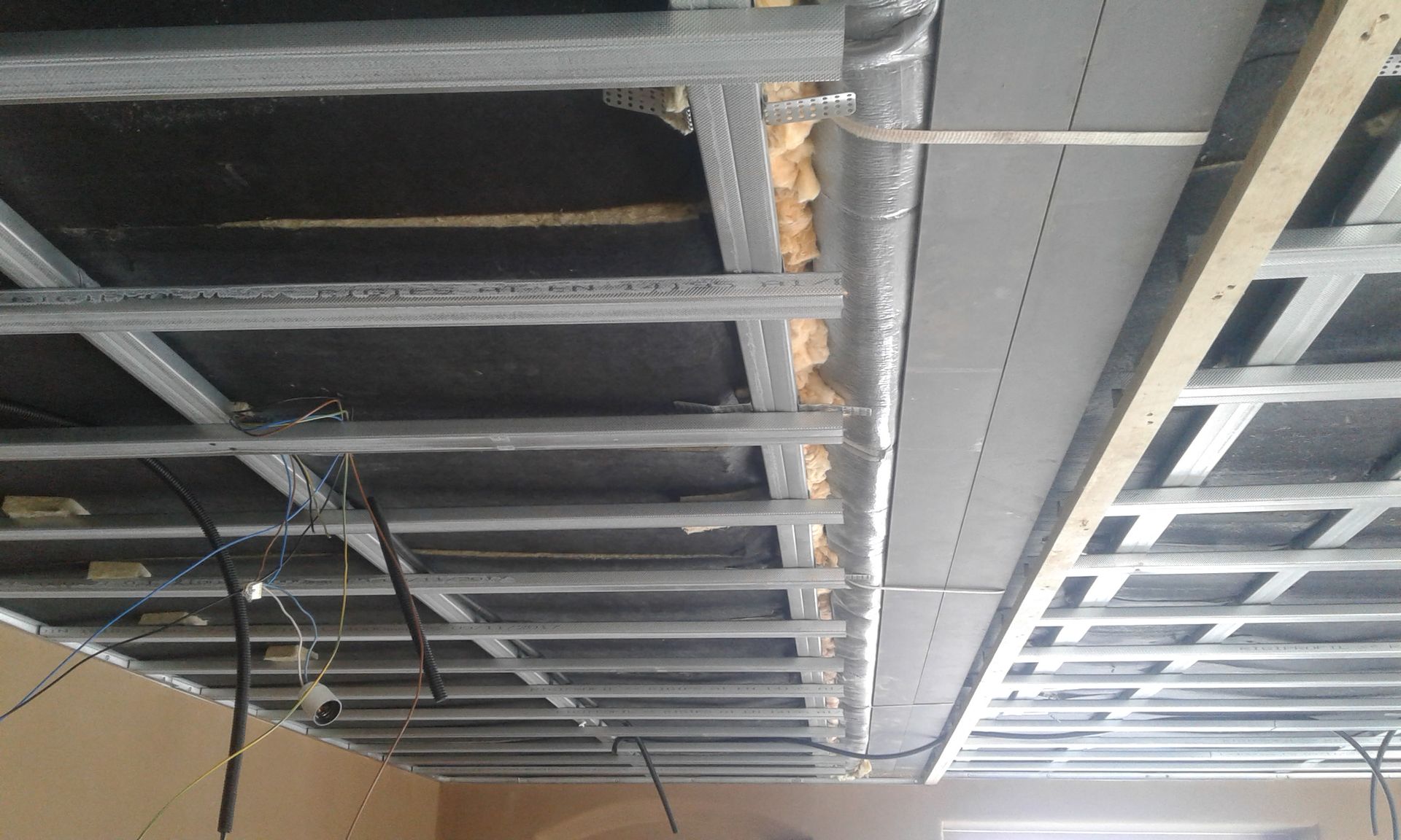 Metallrahmendecke im Bau, mit Isolierung und freiliegenden Leitungen.