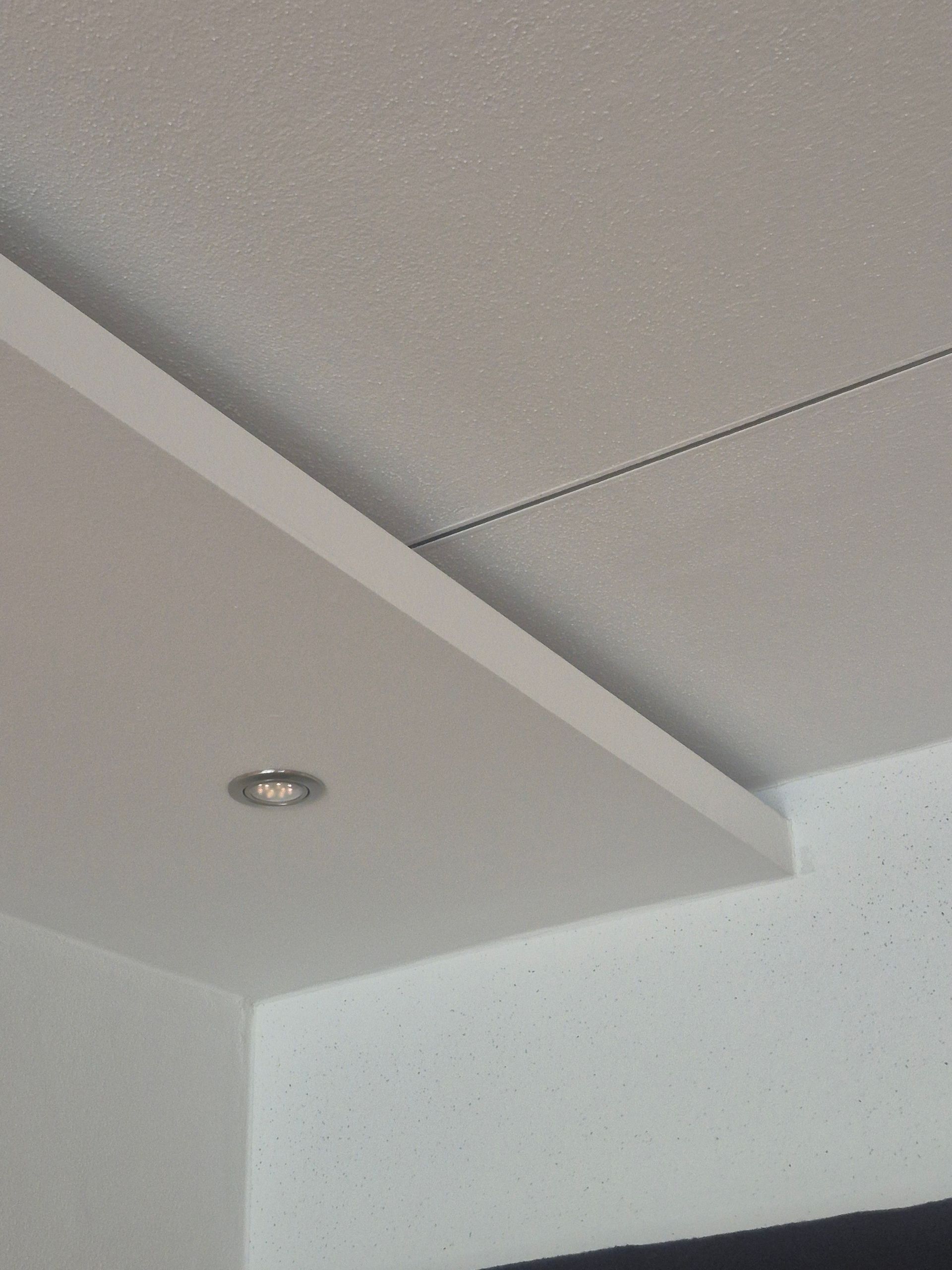 Weiße Decke mit Einbauleuchte und herunterklappbarem Abschnitt.