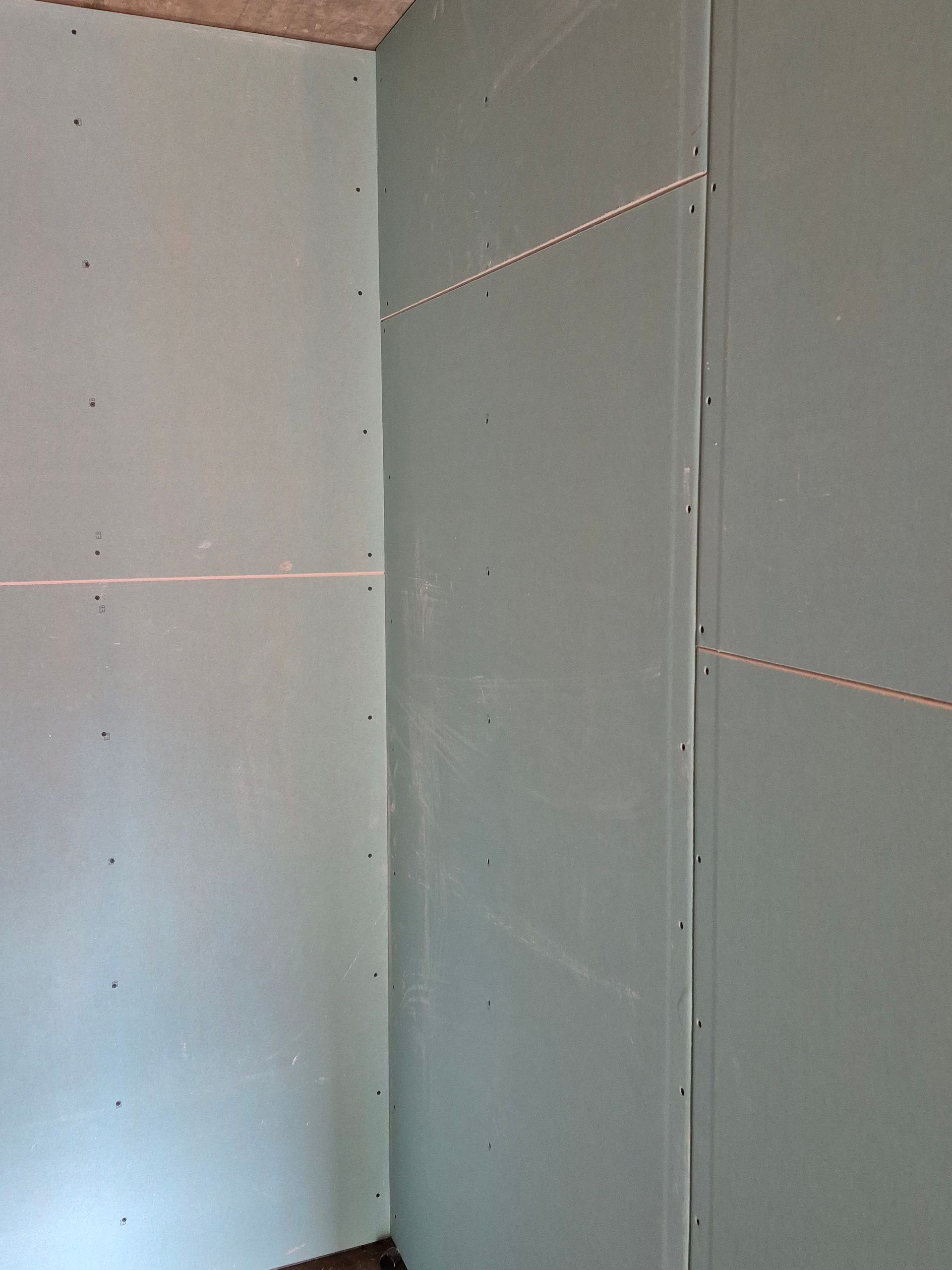 Ecke einer mit Gipskartonplatten verkleideten Wand, hellblau-grüne Farbe, mit sichtbaren Nähten und Schraubenköpfen.