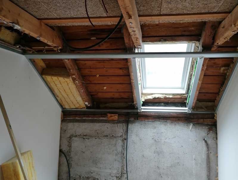 Innenansicht eines unfertigen Raumes mit einem Oberlicht in der Decke und freiliegenden Holzbalken.