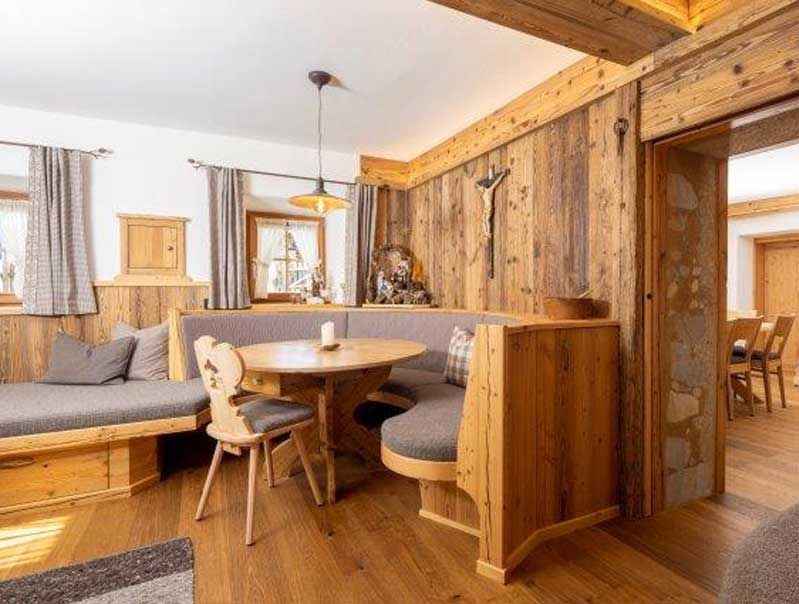 Gemütlicher, rustikaler Essbereich mit Holzwänden, eingebauten Sitzgelegenheiten, rundem Tisch und einem Kruzifix.