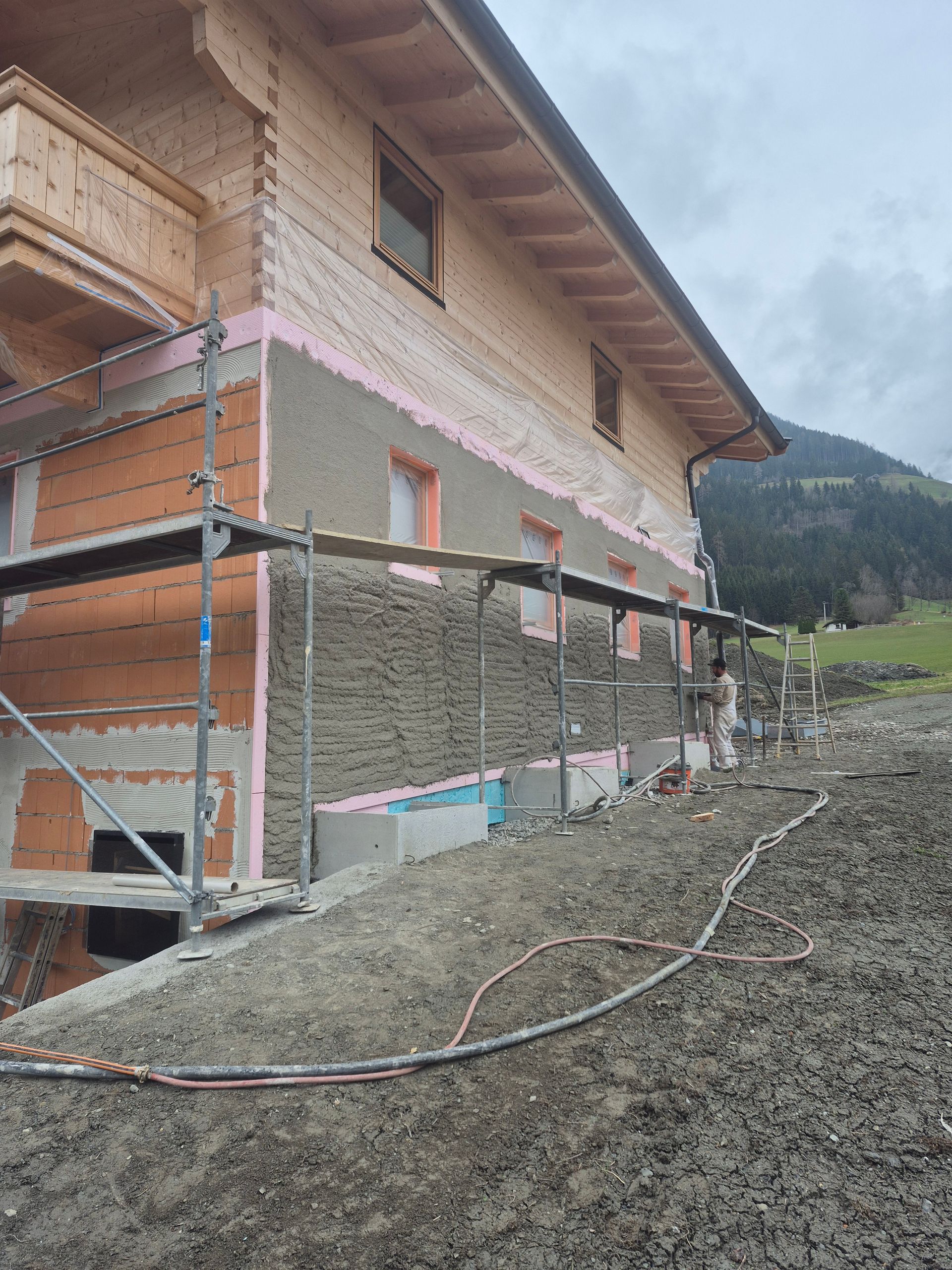Bau einer Hausfassade mit Gerüst und Isolierung. Die Fassade besteht aus Ziegeln und Holz. 