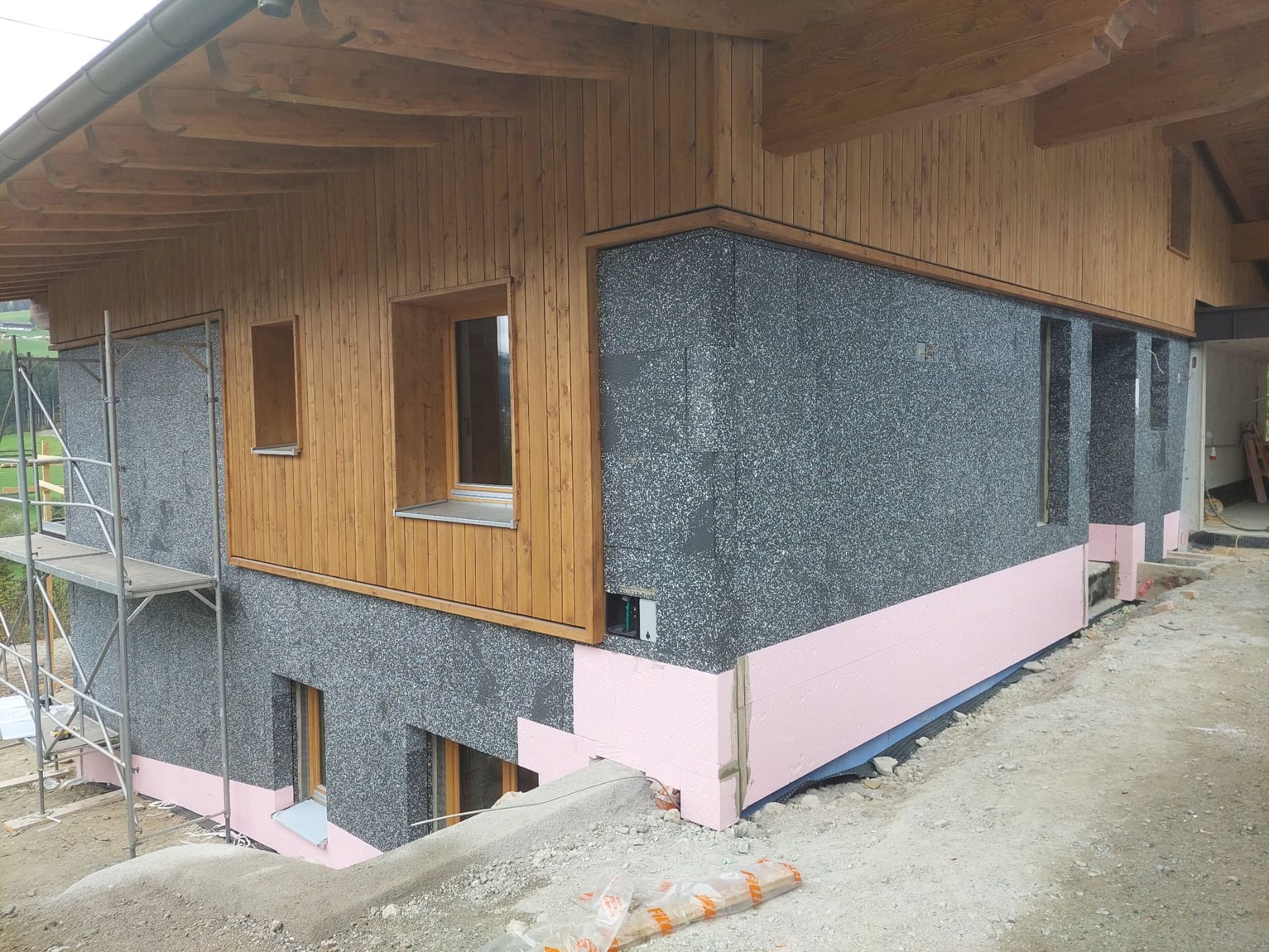 Gebäudeaußenseite mit Holzverkleidung, grau strukturierten Wänden, rosa Isolierung und Fenstern, im Bau.