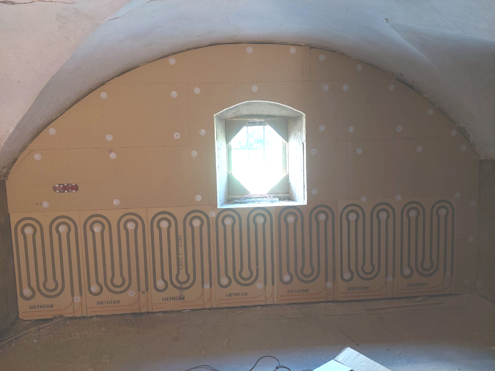 Im Bau befindlicher Raum mit gewölbter Decke, Fenster und installierten Fußbodenheizungselementen.