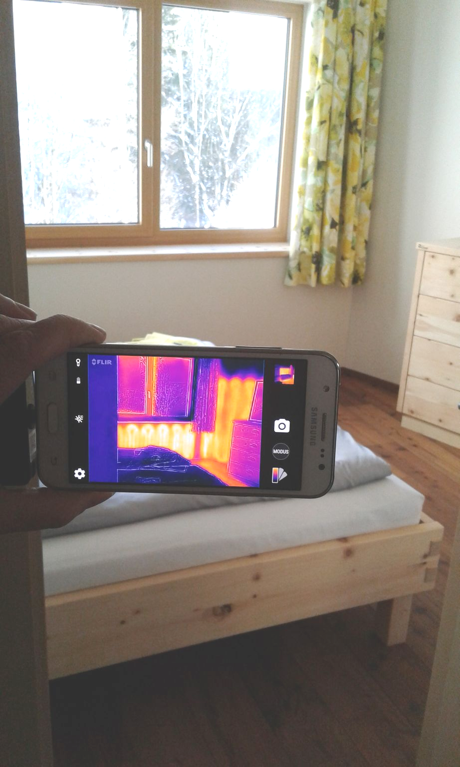 Person hält ein Telefon, auf dem ein Wärmebild eines Raums angezeigt wird.Wärmeverteilung mit SIETHERM.