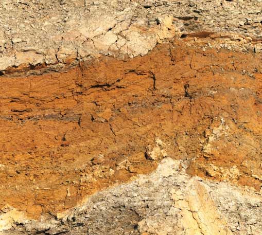 Geschichtete Erde mit einem markanten orangefarbenen Band, das möglicherweise auf Eisenoxid hinweist.