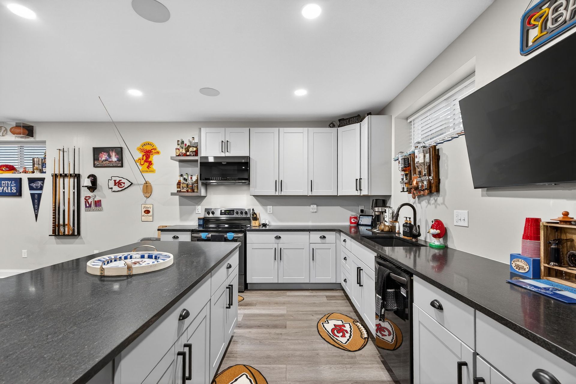 A basement kitchen featuring white cabinets, dark countertops, a large island, and sports-themed wall decor.