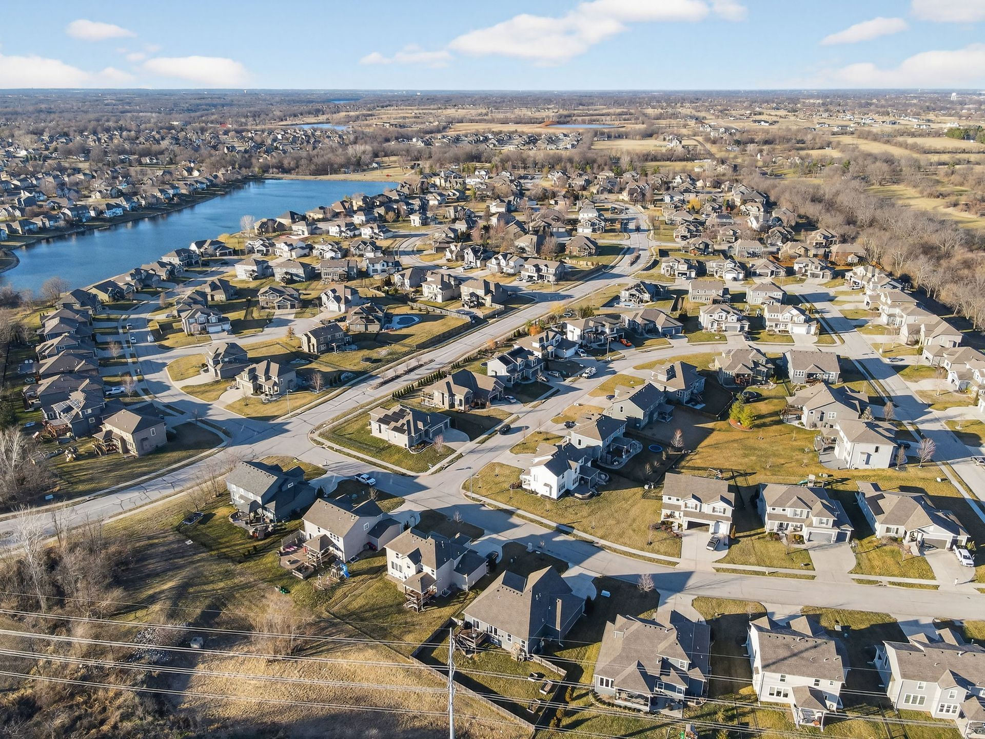 Aerial view of a dense suburban neighborhood with many detached houses, paved roads, and a blue lake on the left.