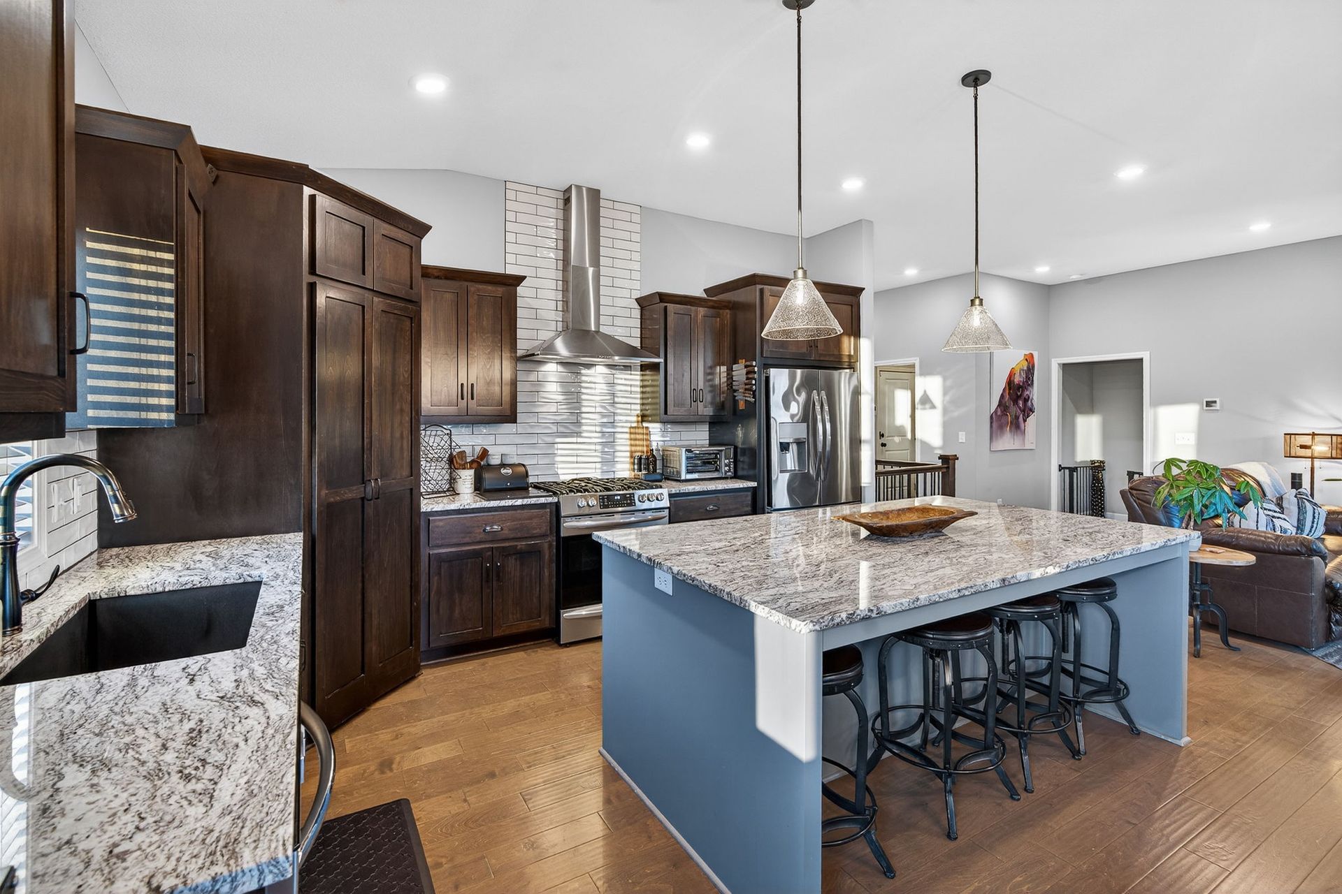 A modern kitchen featuring dark wood cabinets, granite countertops, a blue island with bar stools, and stainless appliances.