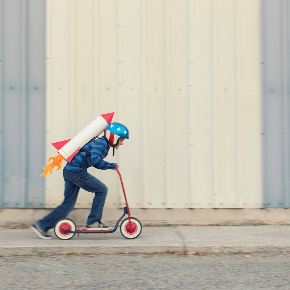 A young boy is riding a scooter with a rocket on his back