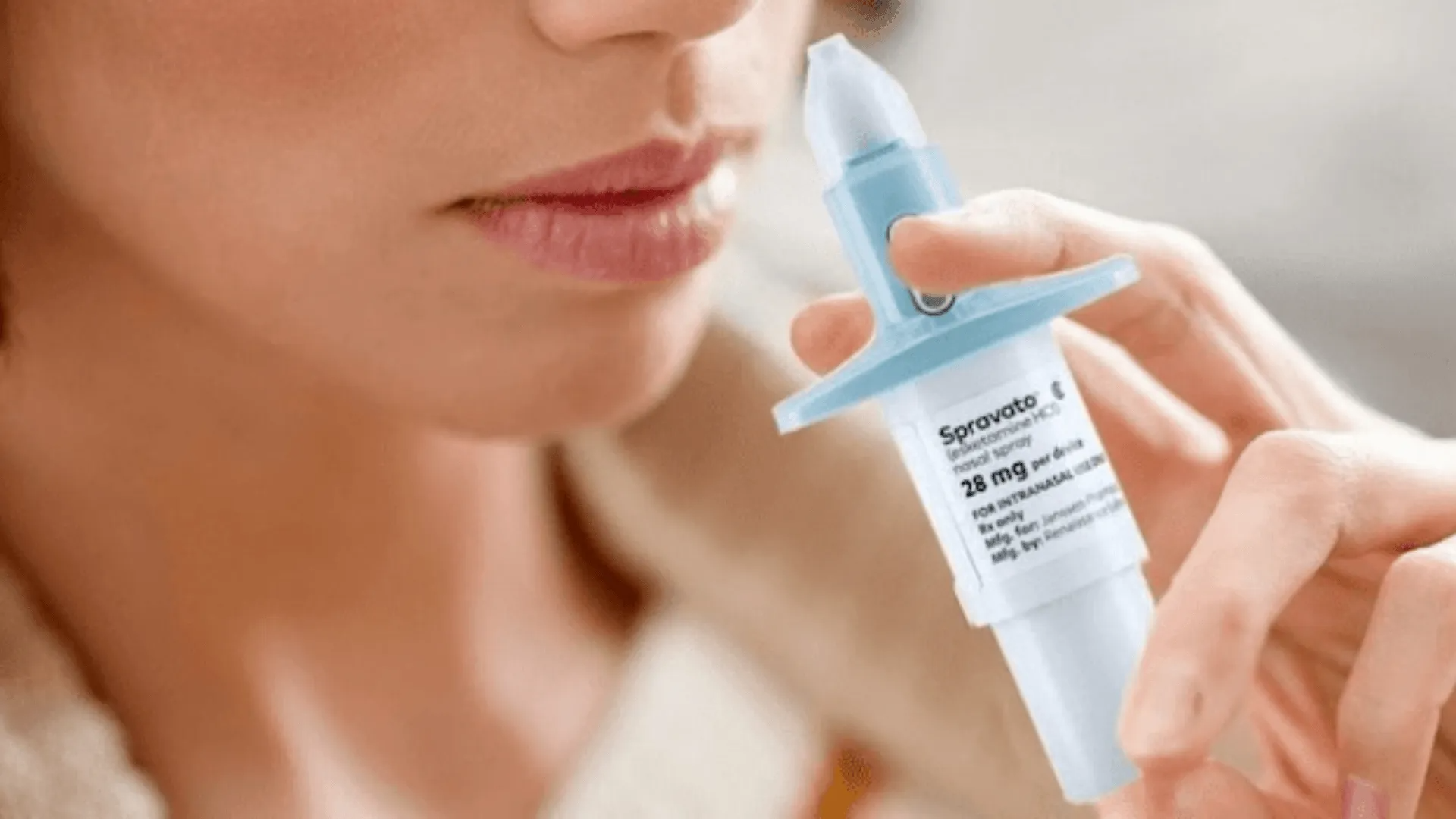 Person holding a blue nasal spray near their nose in a close-up view.