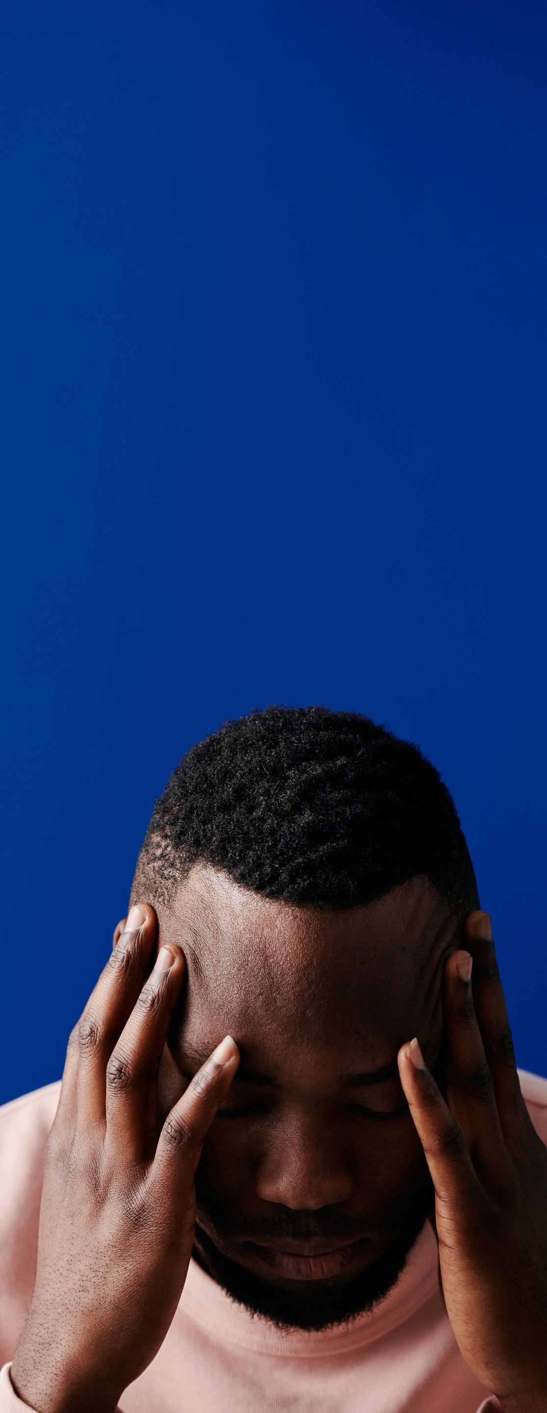 Man holding his head in stress against a blue background