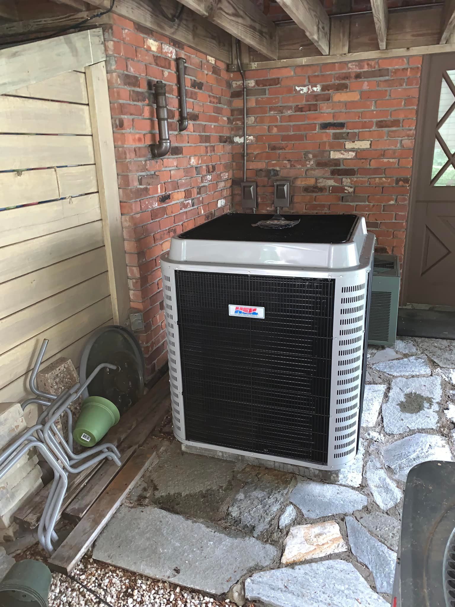 A large air conditioner is sitting in a garage next to a brick wall.