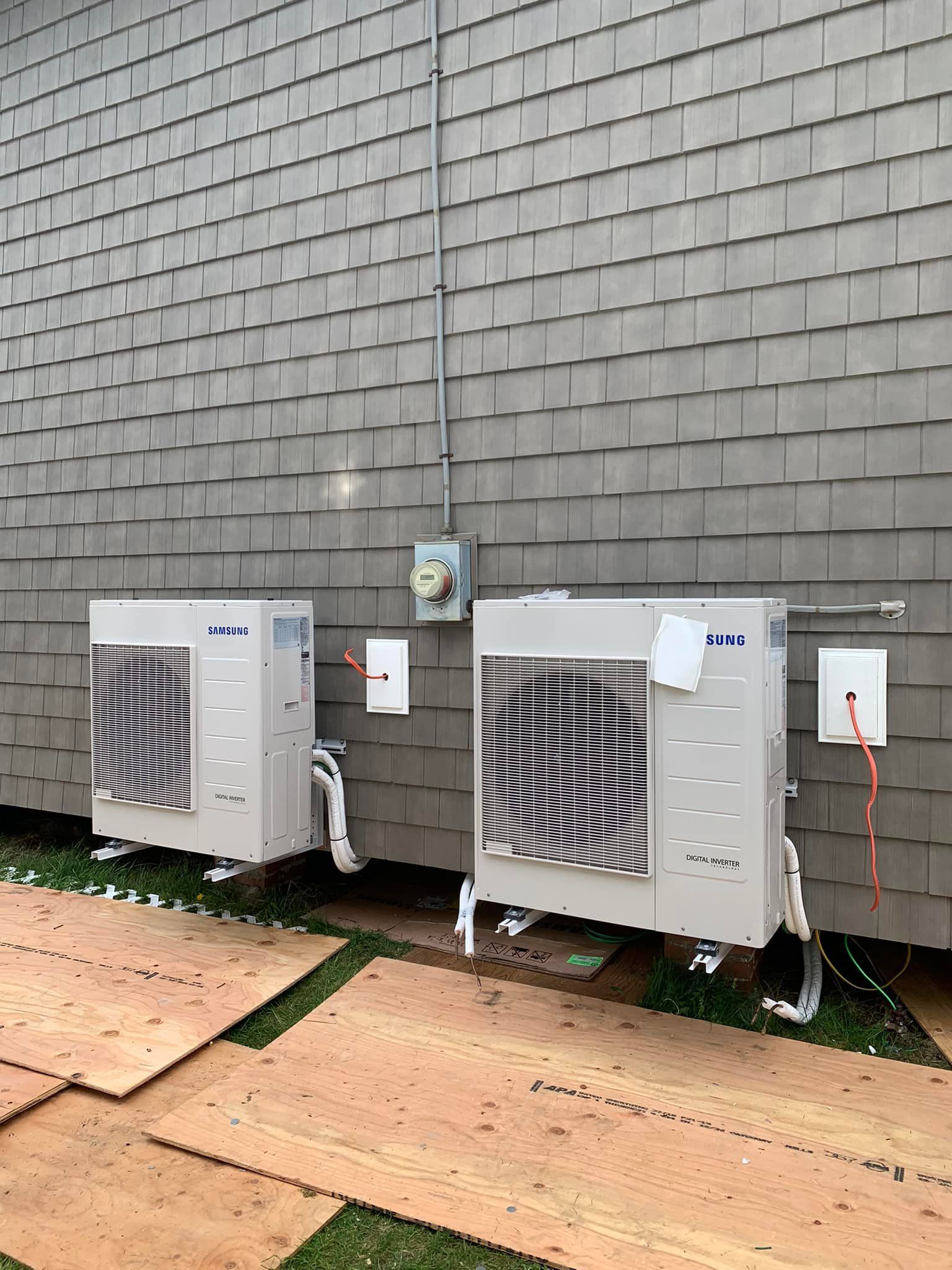 Two air conditioners are sitting on the side of a brick building.