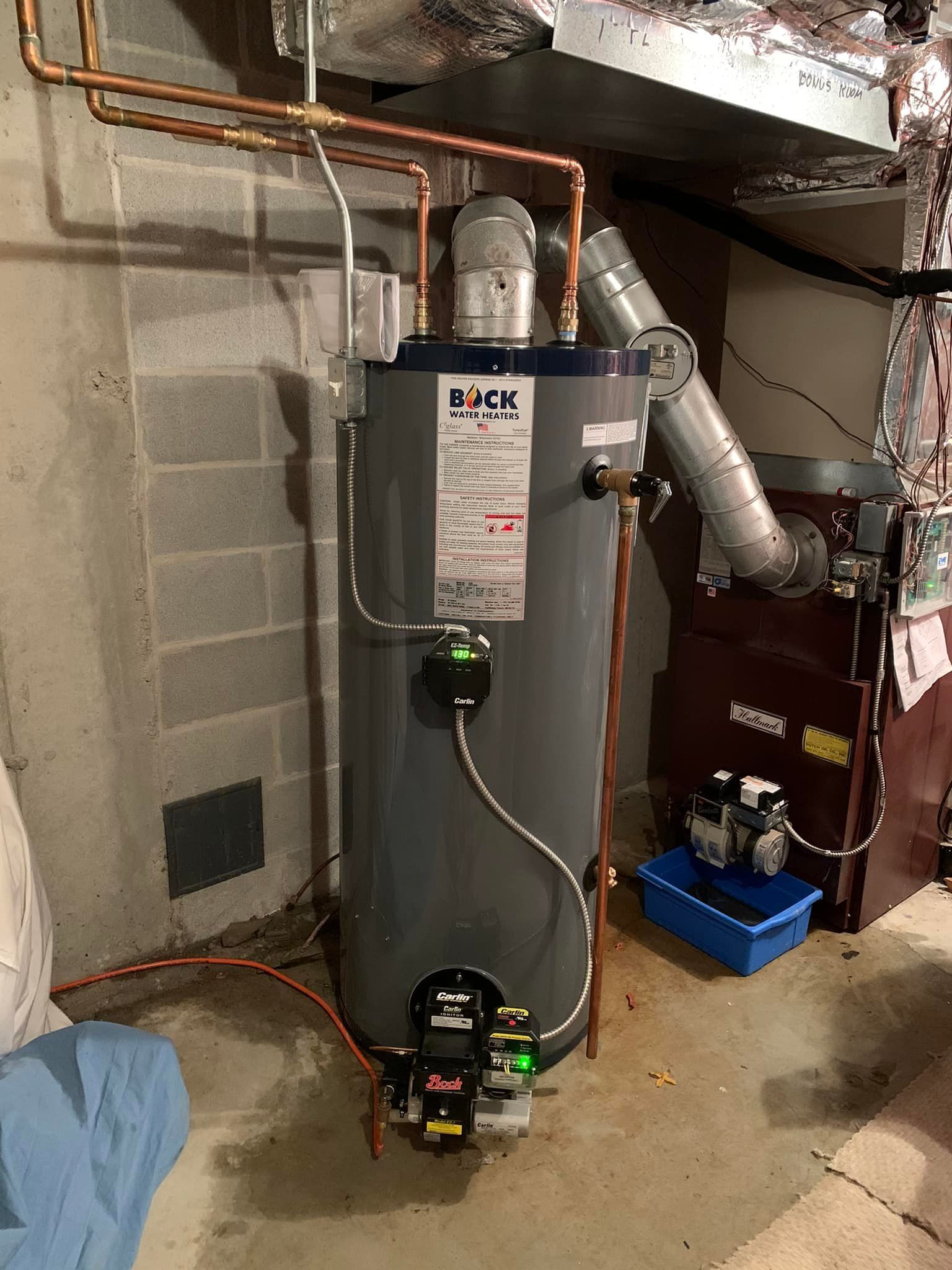 A water heater is sitting in a basement next to a furnace.