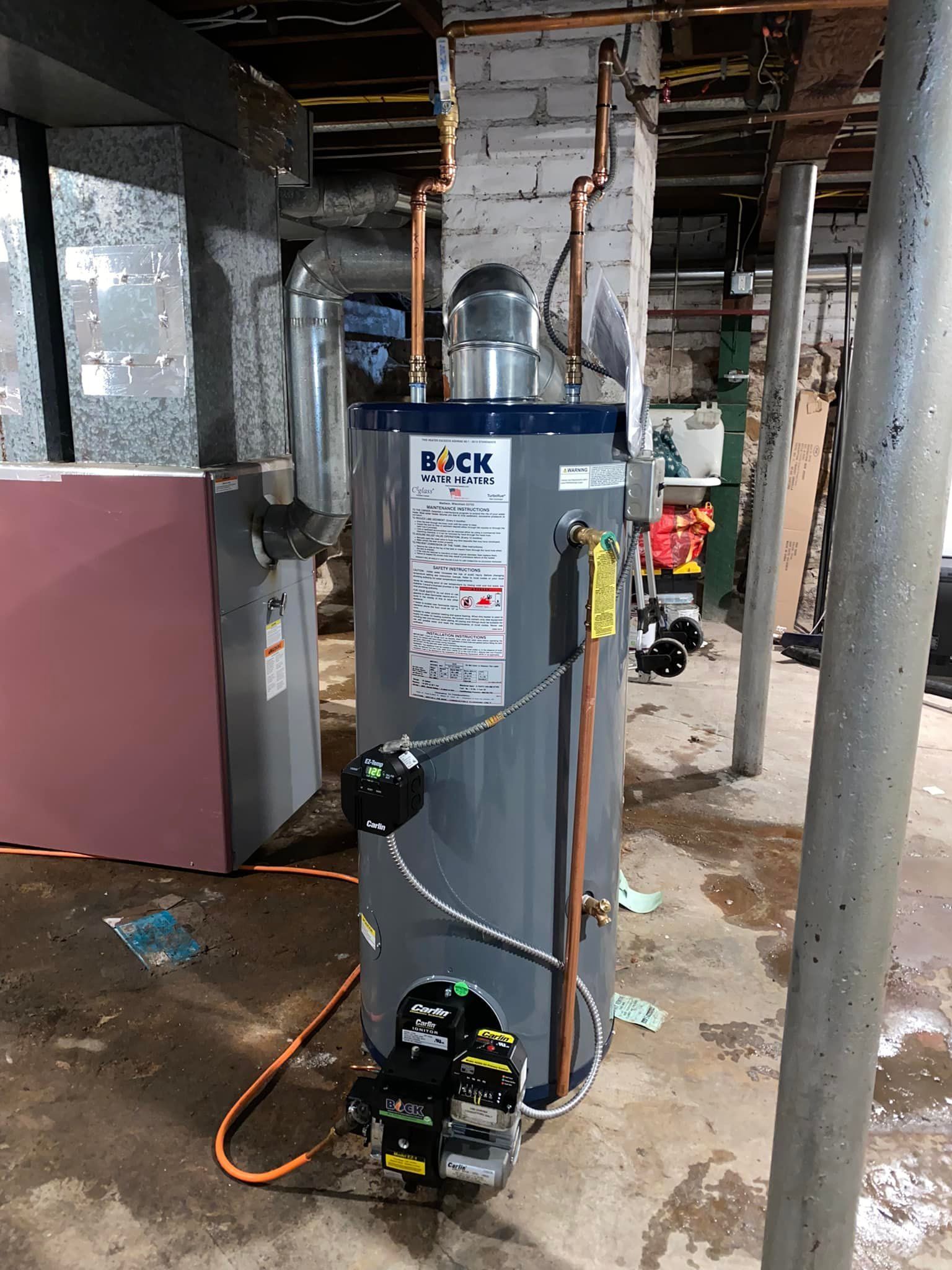 A water heater is sitting in a basement next to a furnace.
