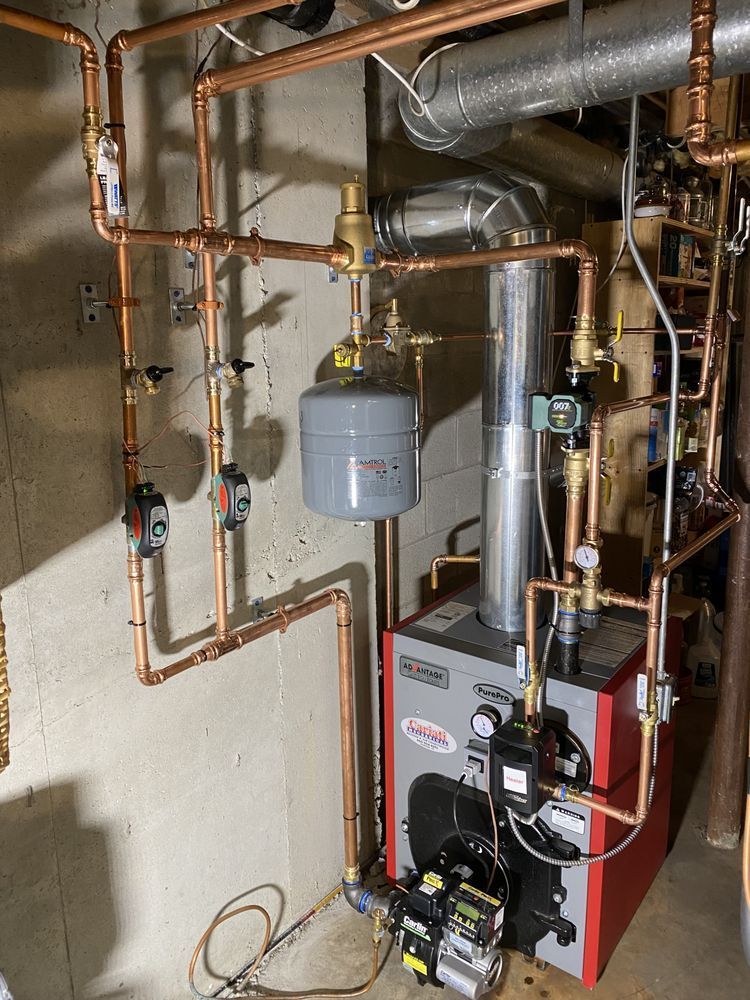 A boiler is sitting in a basement surrounded by pipes.