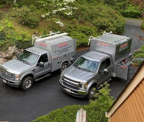 Two trucks are parked in a driveway next to a house.